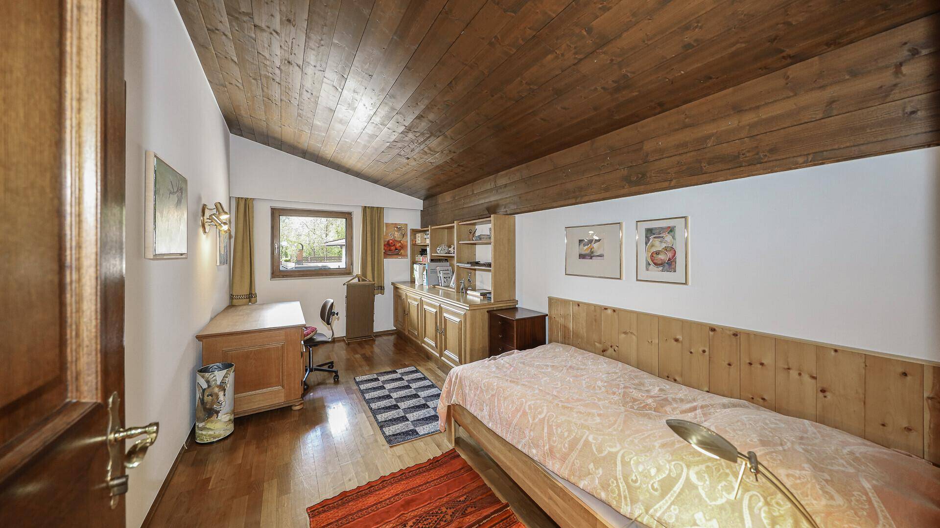 Gemütliches Zimmer mit Holzdecke, Schreibtisch und Einzelbett.