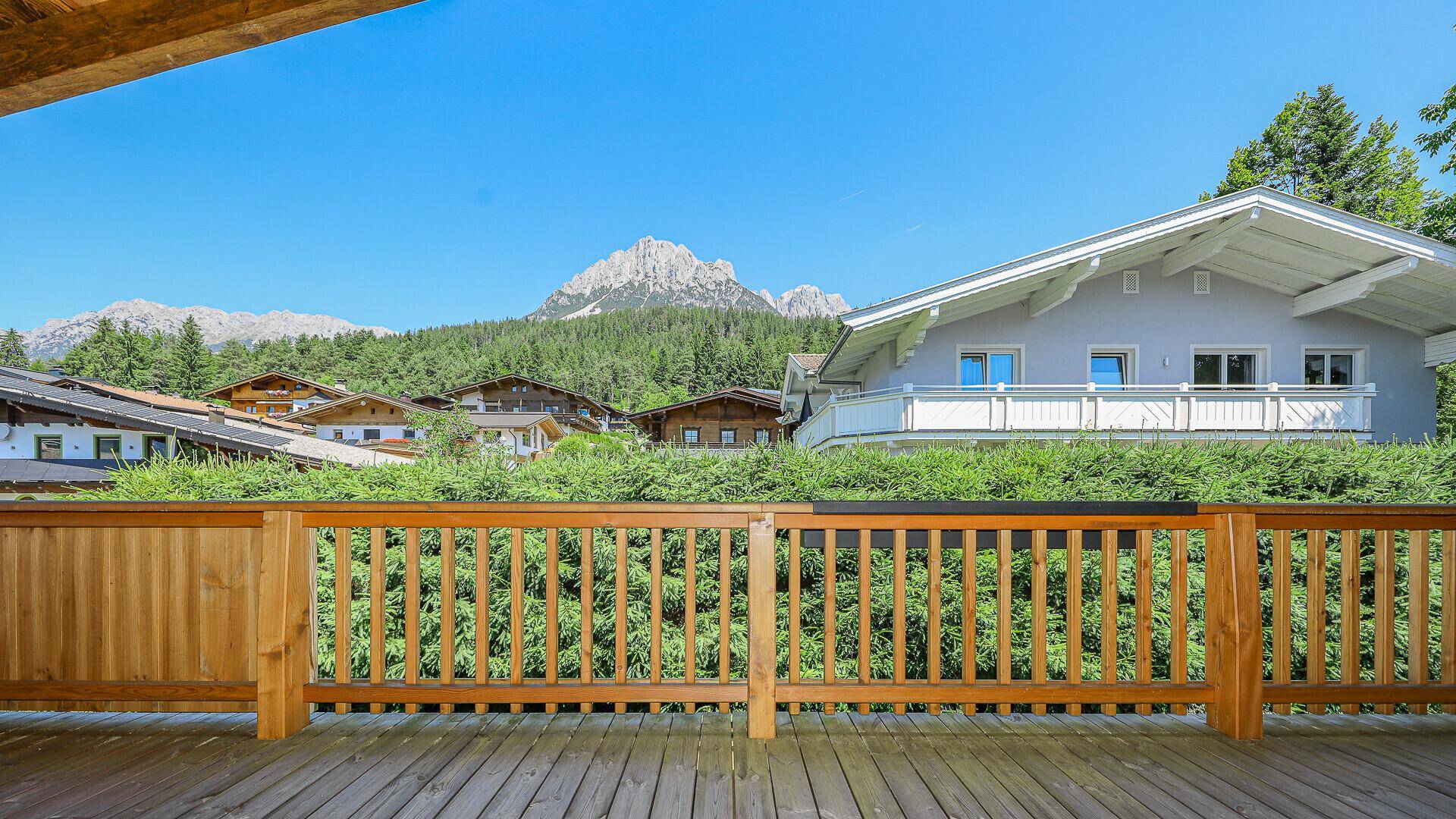 Balkon mit Holzgeländer und Blick auf die majestätischen Berge und grüne Umgebung.