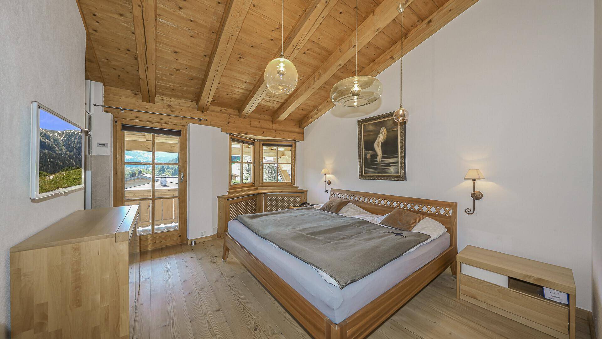 Gemütliches Schlafzimmer mit Holzbalkendecke, Holzboden und Zugang zu einem Balkon.
