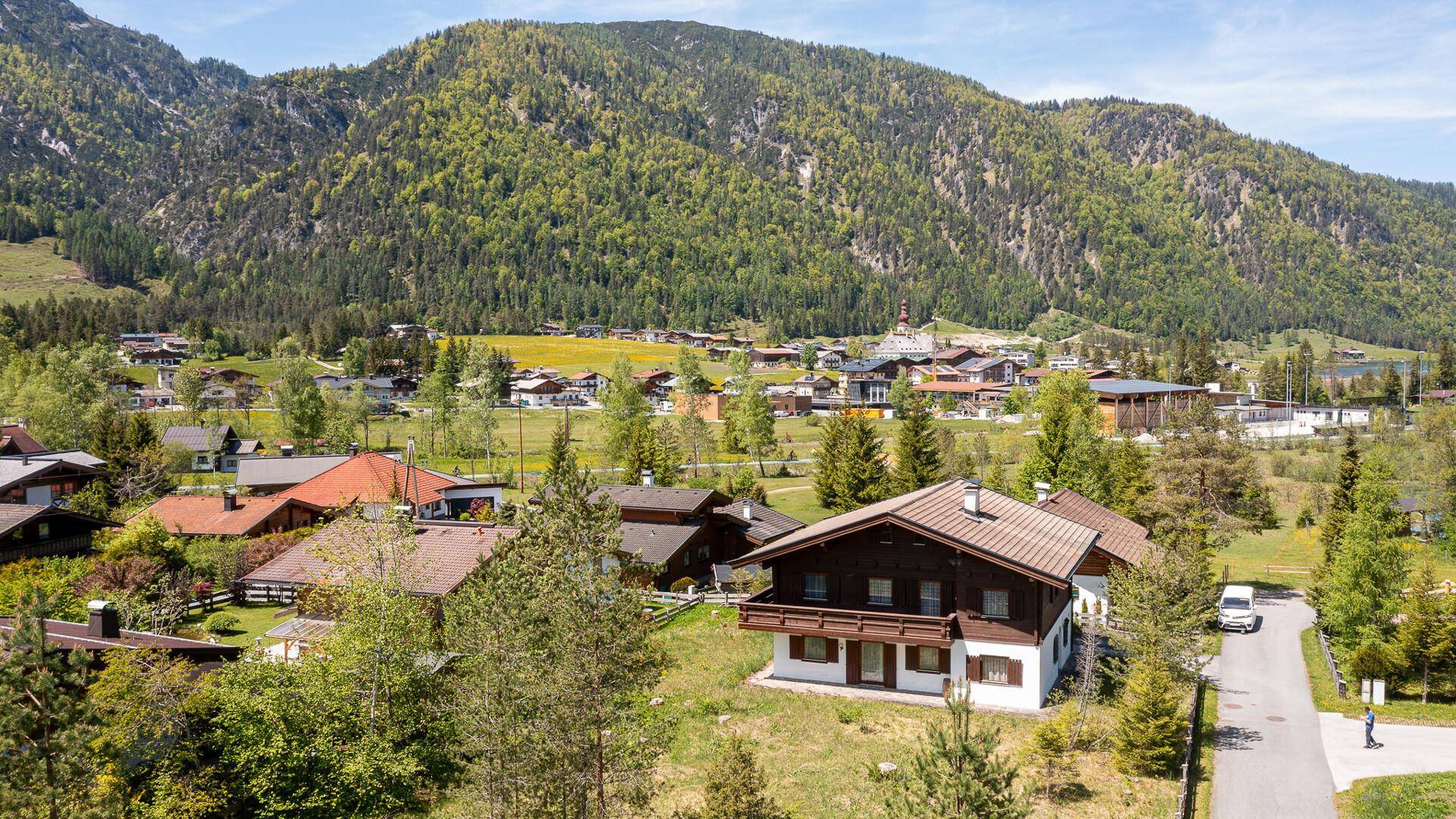 Luftaufnahme eines malerischen Dorfes mit traditionellen Häusern, umgeben von grünen Bergen und Wäldern.