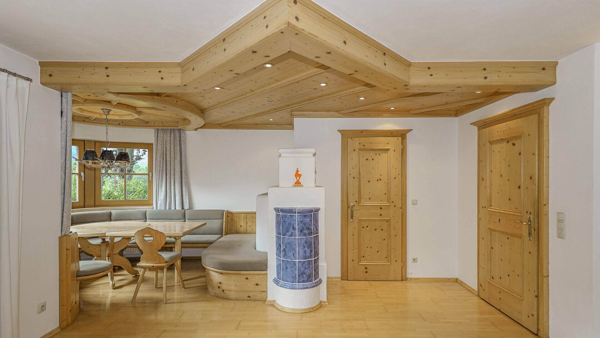 Traditioneller Essbereich mit Holztisch, Eckbank und einem dekorativen Kachelofen.