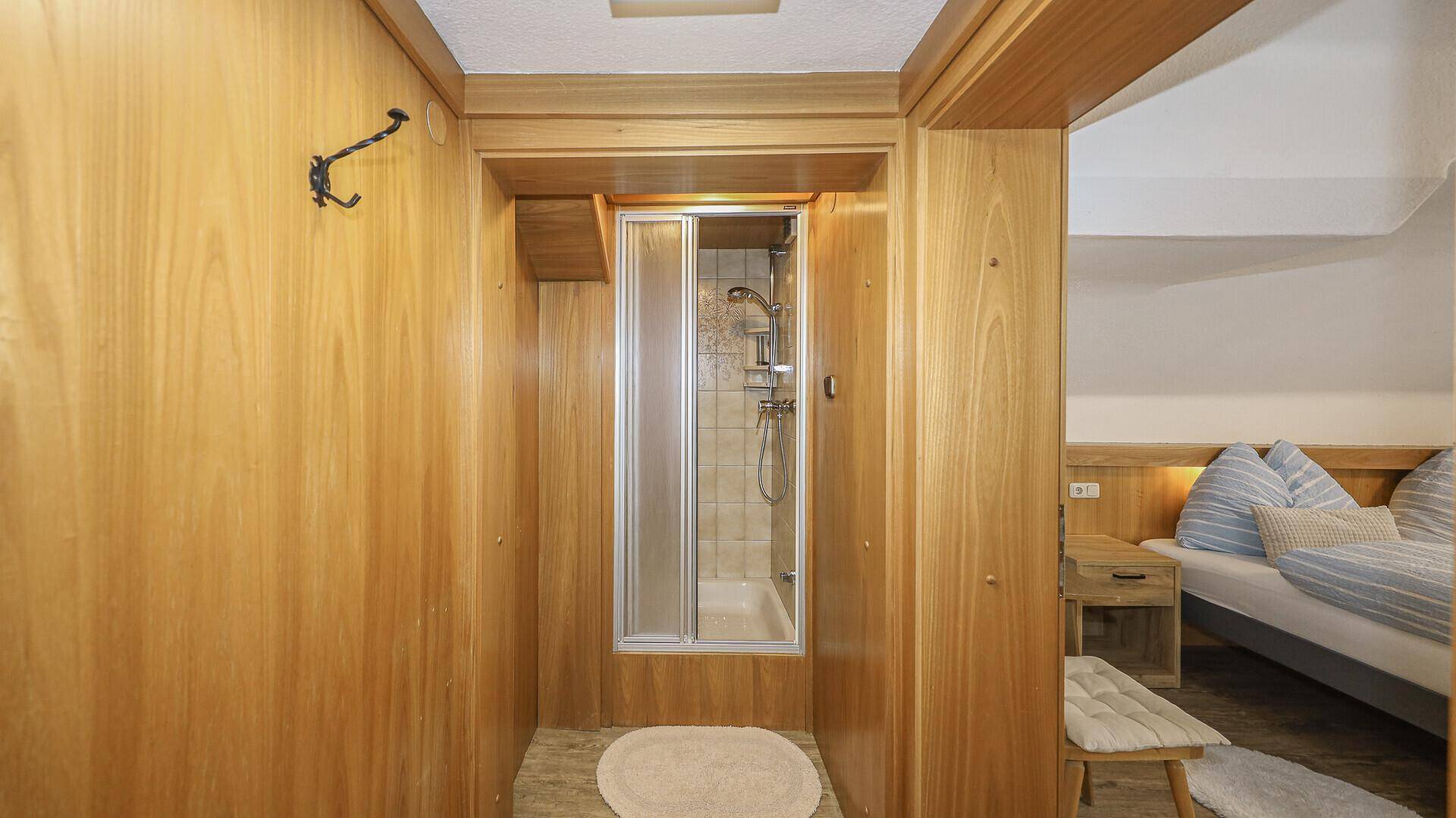Kleiner Duschbereich in einem Holzvertäfelten Flur, angrenzend an ein Schlafzimmer.