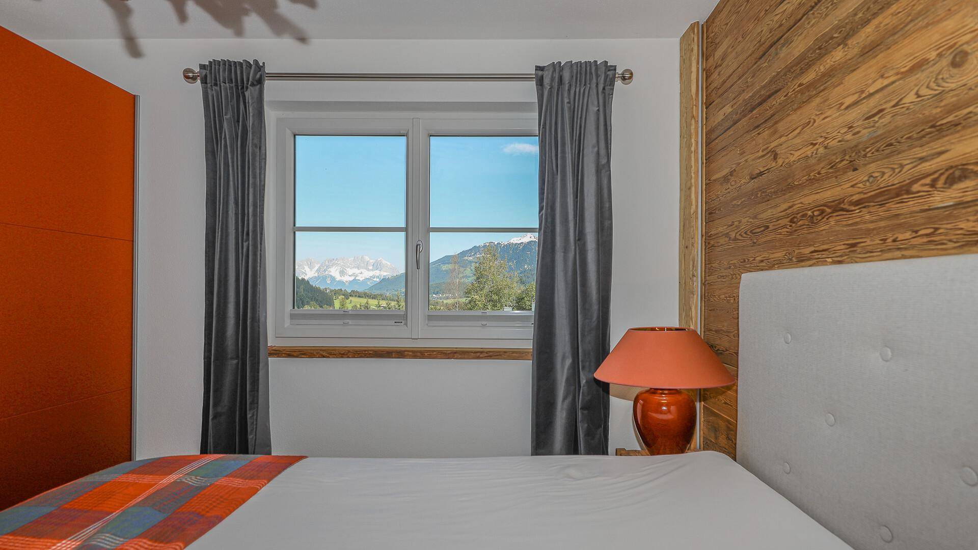 Schlafzimmer mit Doppelbett und Fenster, das einen atemberaubenden Blick auf die Alpen bietet.