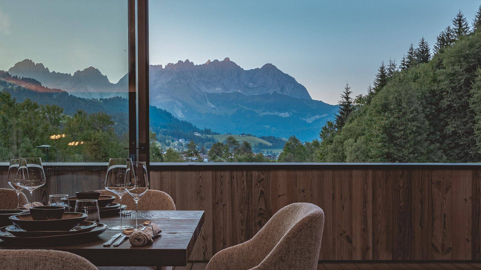 Essbereich mit Holzwänden und Panoramafenstern, die einen atemberaubenden Bergblick bieten.