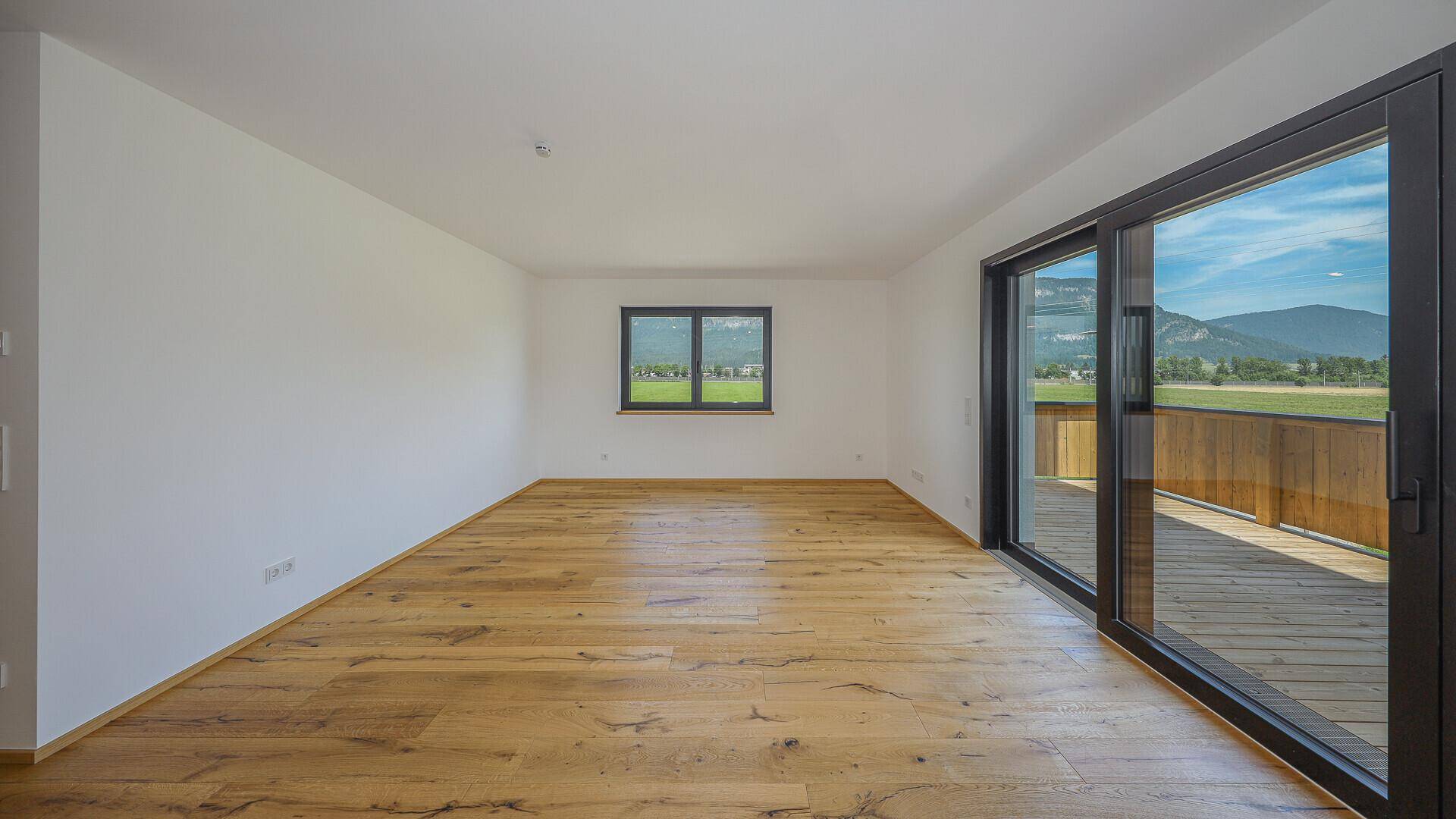 Geräumiger, unmöblierter Raum mit Holzboden und Zugang zu einem Balkon mit Bergblick.