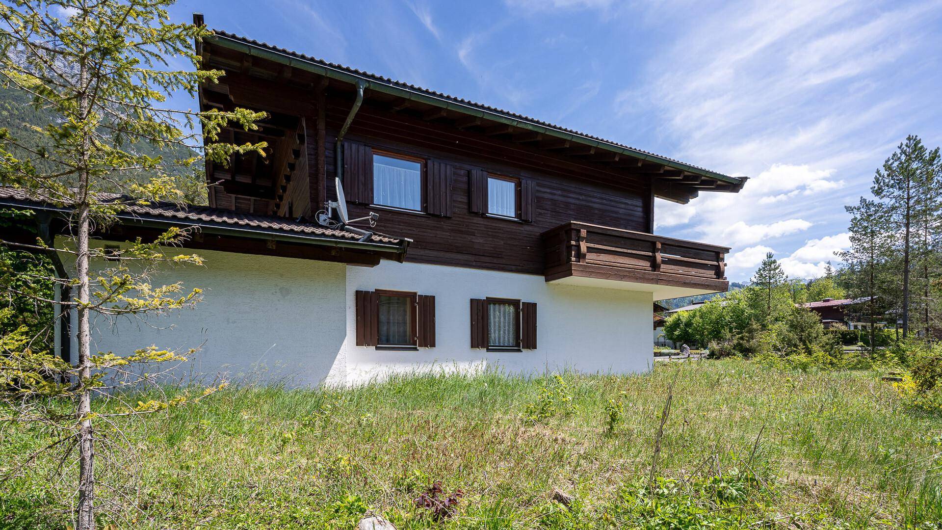 Seitenansicht eines traditionellen Chalets mit Holzbalkon und weißer Fassade in ländlicher Umgebung.