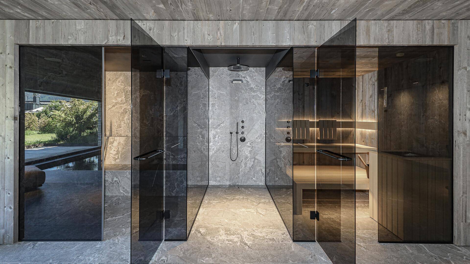 Moderner Wellnessbereich mit Regendusche und Sauna, umgeben von eleganten Glaswänden.