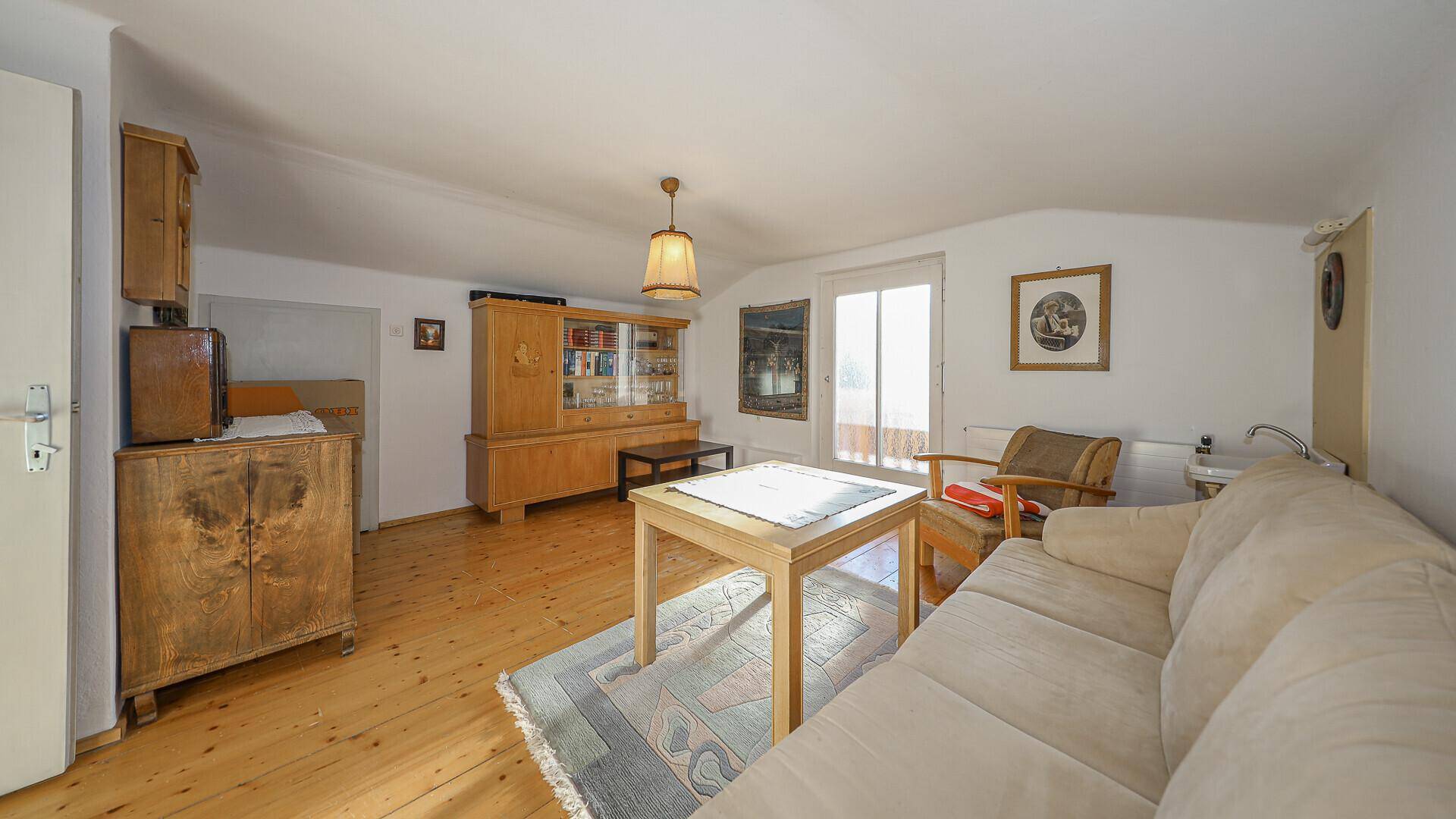 Wohnzimmer mit Holzboden, Sofa und traditionellen Möbeln, hell durch Balkonzugang.