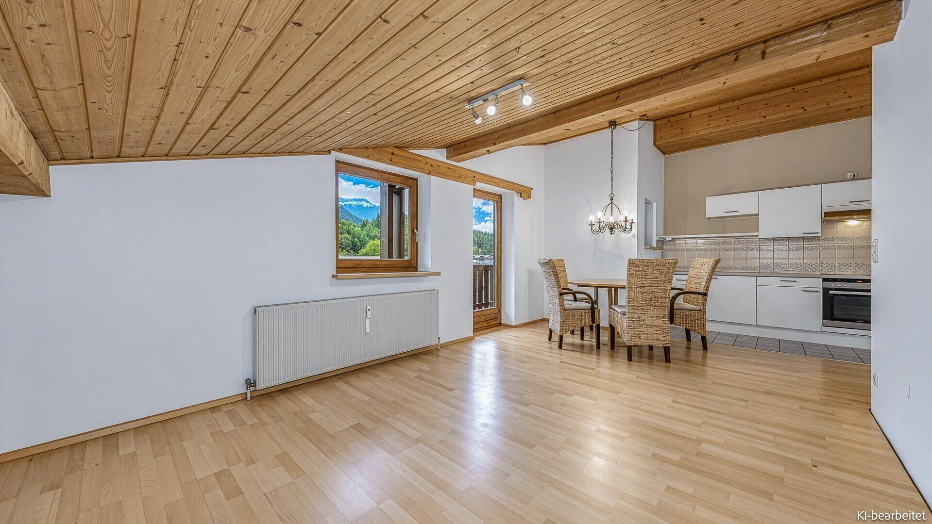 Lichtdurchfluteter Wohn-Essbereich mit Bergblick, Holzbalkendecke und Zugang zum Balkon.