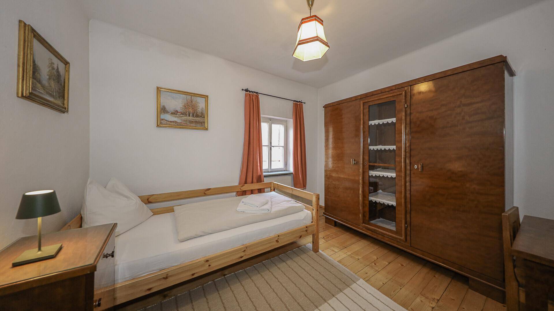 Einfaches Schlafzimmer mit Einzelbett, Holzschrank und Holzboden.