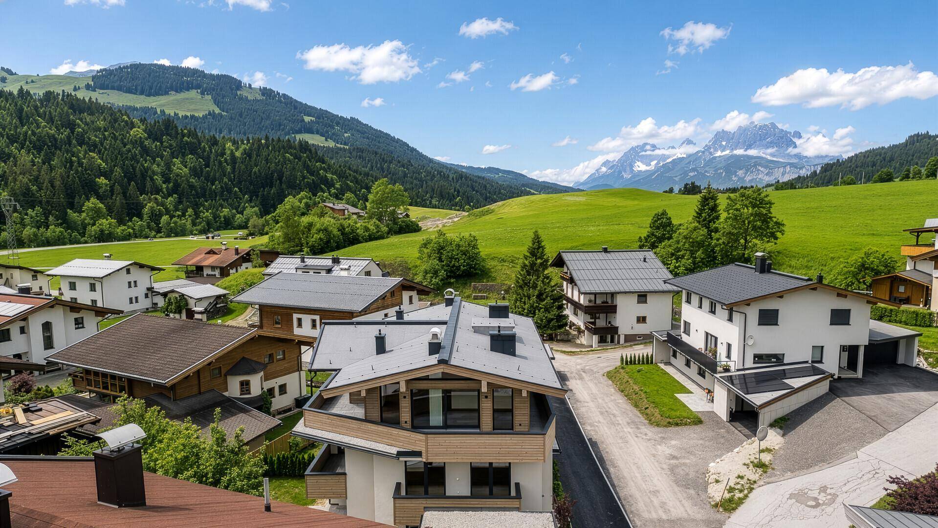 Panoramablick auf eine Wohnsiedlung mit grünen Hügeln und majestätischen Bergen im Hintergrund.