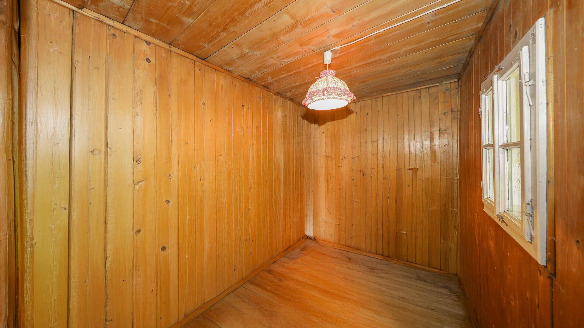 Kleines Schlafzimmer mit Holzverkleidung, Holzdielenboden und einem Fenster.