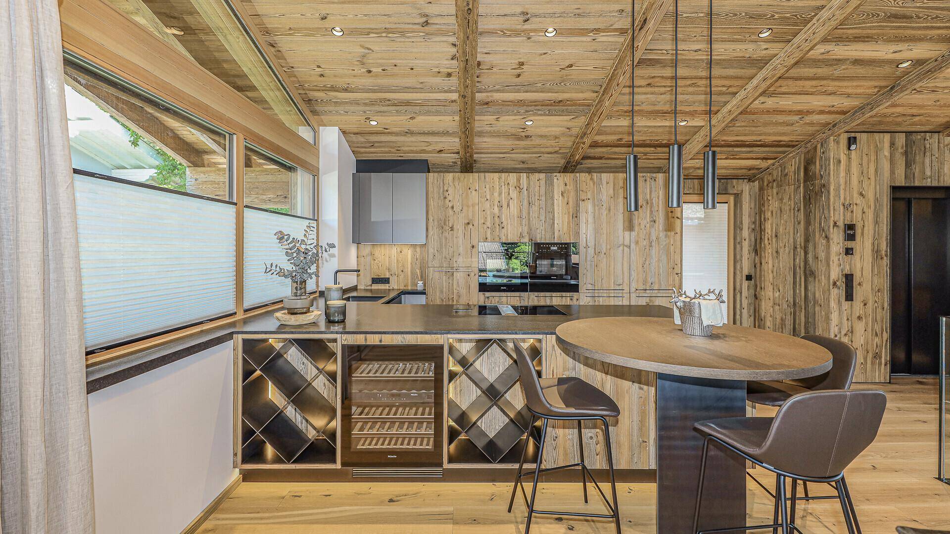 Moderne Küche im alpinen Stil mit Holzelementen, Kochinsel und integriertem Weinkühler.