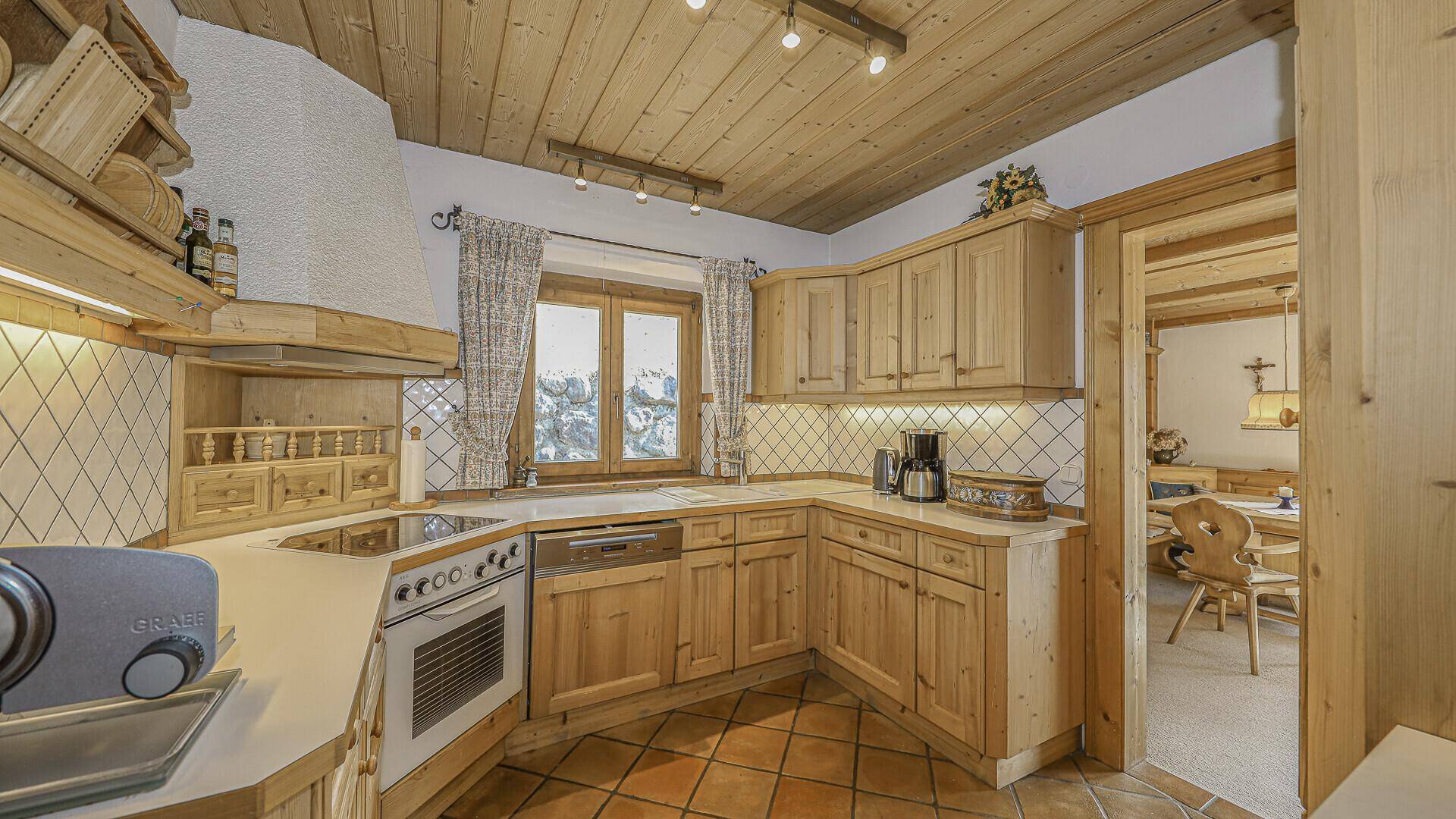 Traditionelle Holzküche mit Einbaugeräten, Fliesenboden und Fensterblick auf die verschneite Landschaft.