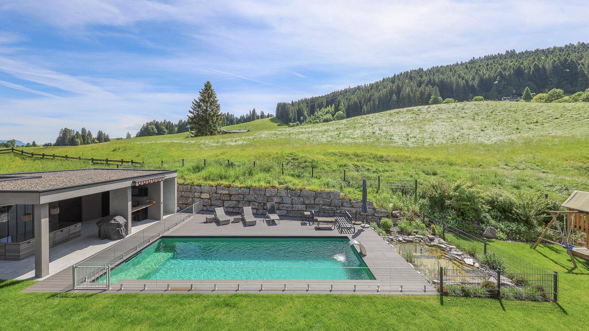 Weitläufiger Außenbereich mit großem Pool, Liegewiese und idyllischer Landschaft im Hintergrund.