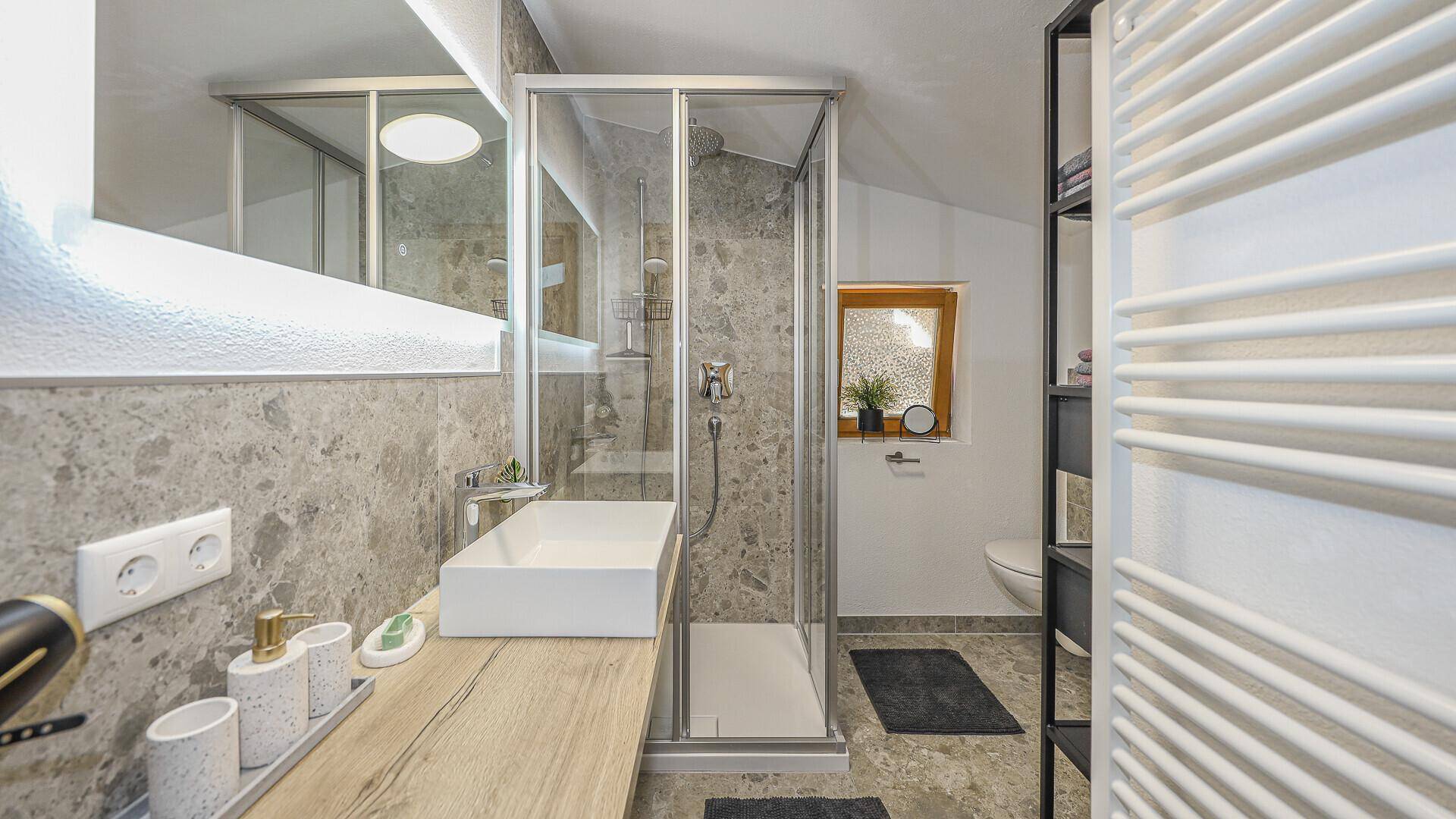 Modernes Badezimmer mit begehbarer Dusche, elegantem Waschbecken und beheiztem Handtuchhalter, hell gefliest.