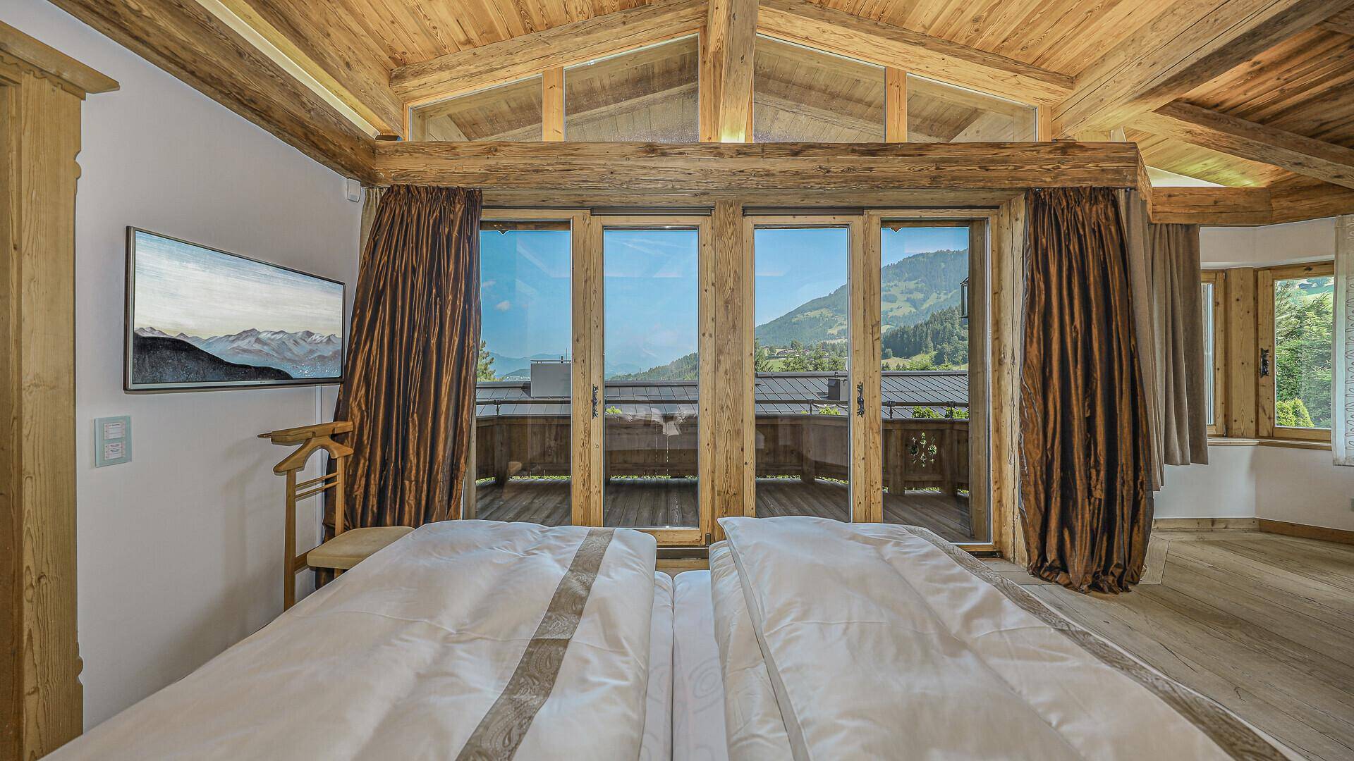 Schlafzimmer mit großen Fenstern, Holzbalken und atemberaubendem Bergblick.