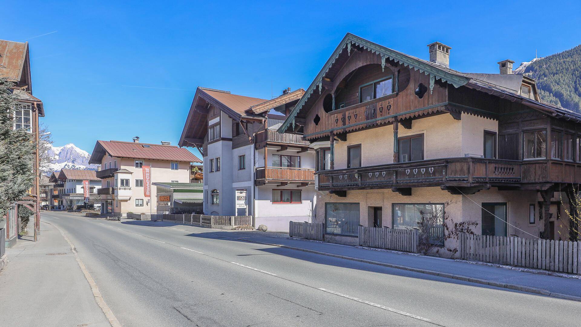 Blick entlang der Straße mit dem traditionellen Gebäude und weiteren Häusern in der alpinen Umgebung.