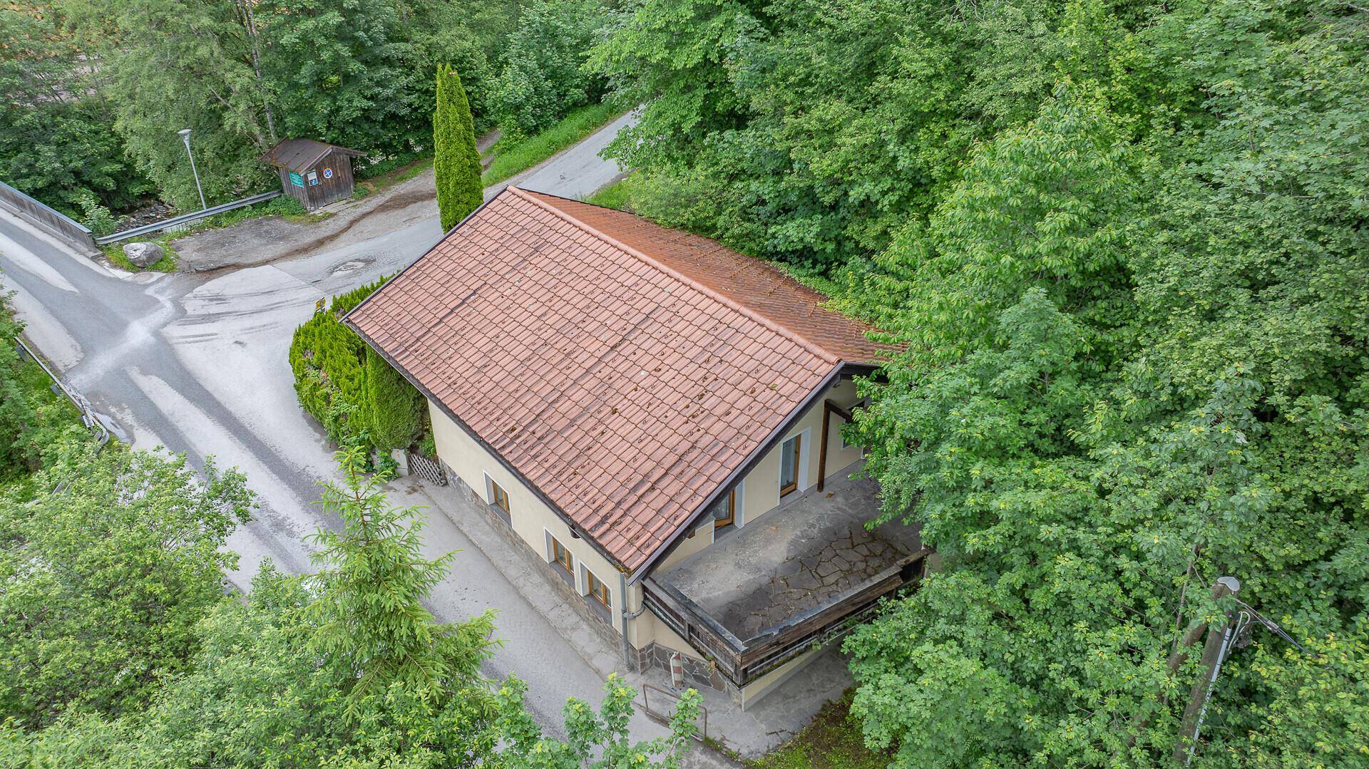 Luftaufnahme eines Hauses mit Ziegeldach, umgeben von dichtem Grün und einer Straße.