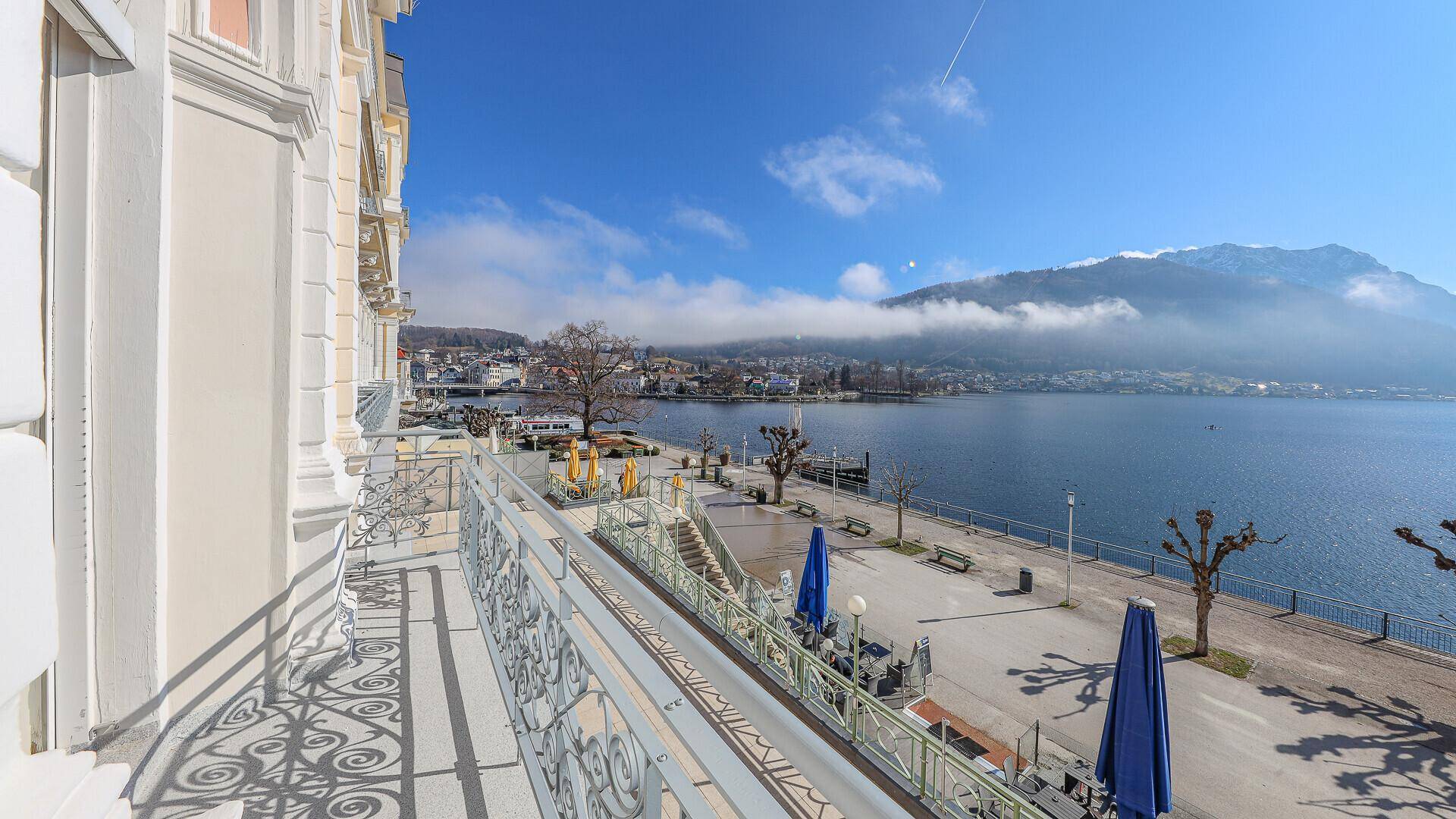 Balkon mit Panoramablick auf den See, die Berge und die belebte Uferpromenade.