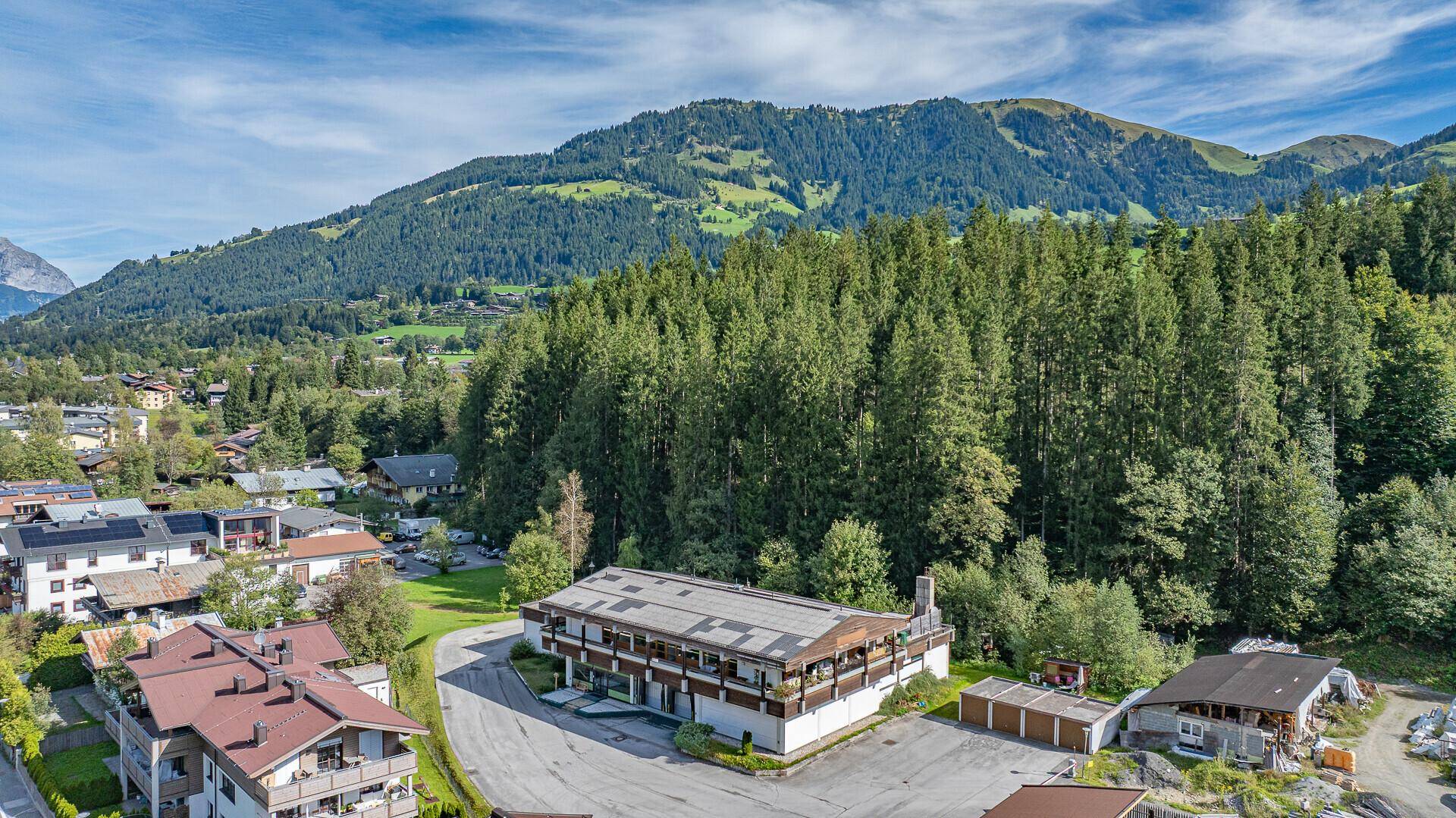 Luftaufnahme des Gebäudes mit Flachdach, umgeben von Wald und Bergen unter blauem Himmel.