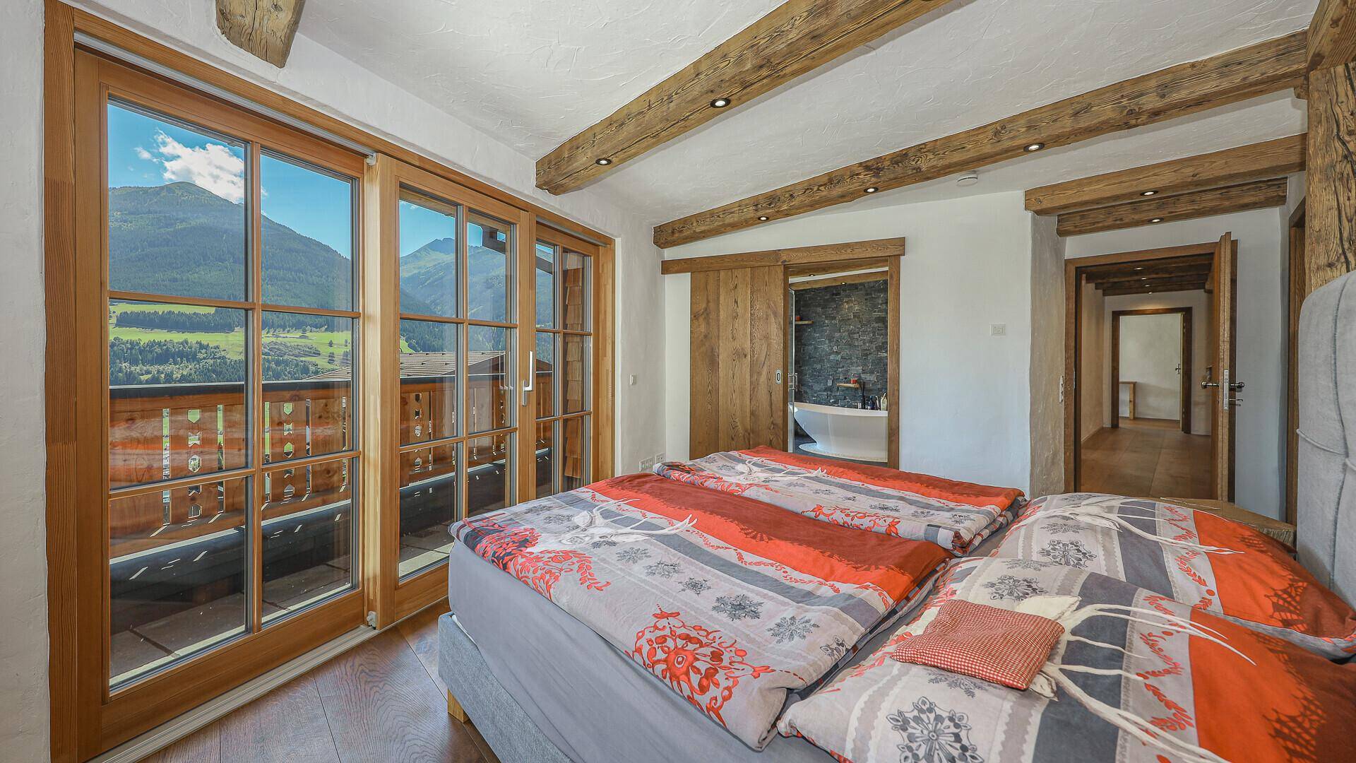 Gemütliches Schlafzimmer mit Holzbalken, Balkonzugang und weitem Blick auf die Berge.