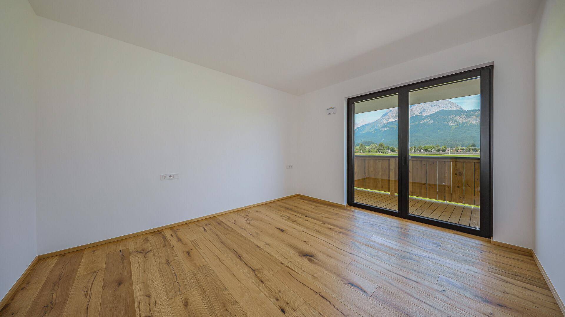 Heller Raum mit Holzboden und großem Fenster, das einen direkten Bergblick ermöglicht.