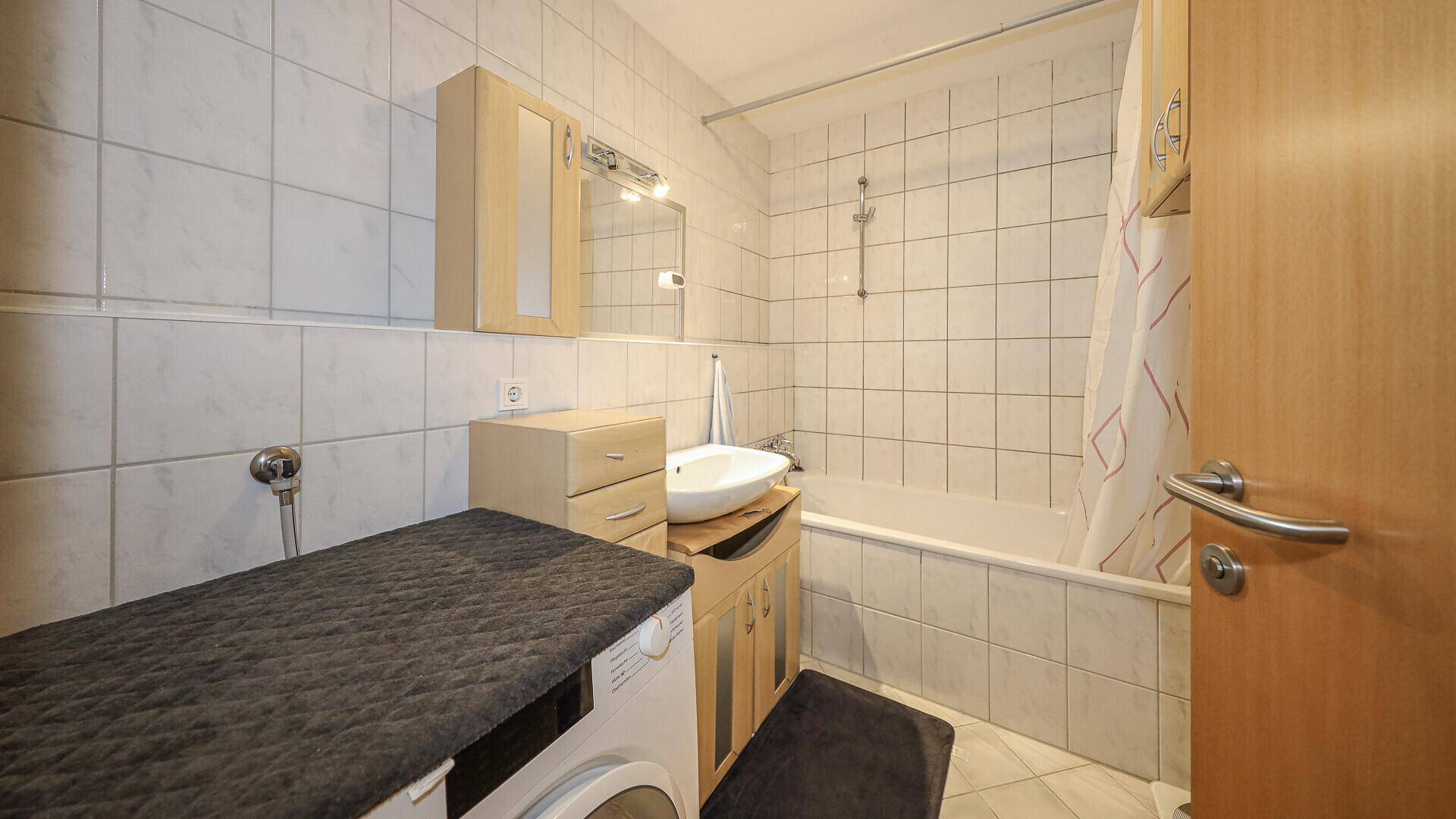 Funktionales Badezimmer mit Badewanne, Waschbecken und Waschmaschine, hell gefliest.