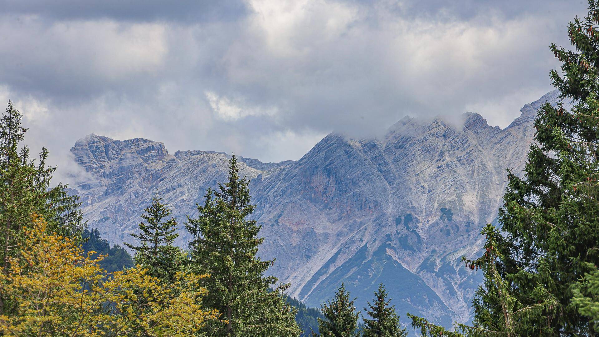 Nahaufnahme der imposanten Bergkette mit Wolken und dichten Wäldern.