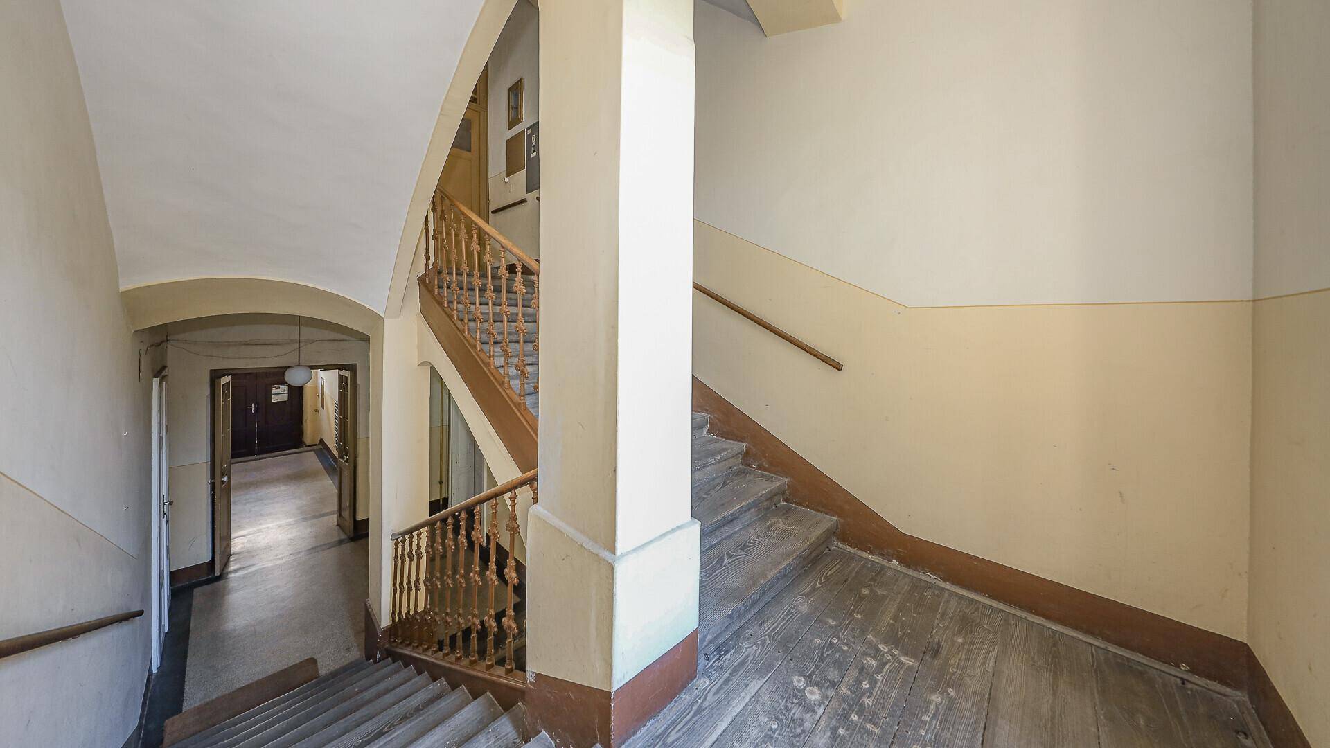 Altes Treppenhaus mit abgenutzten Holzstufen und renovierungsbedürftigen Wänden.
