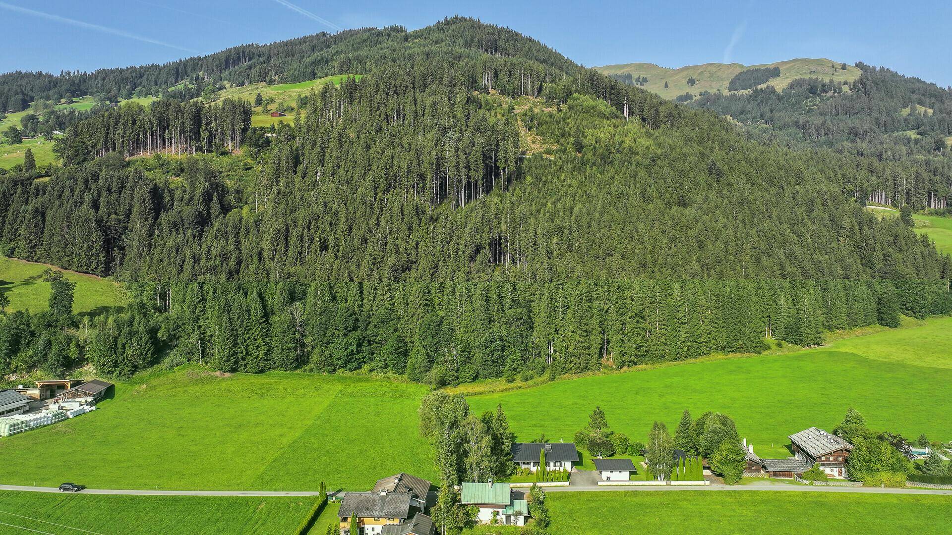 Luftaufnahme des Anwesens in einer weiten grünen Landschaft mit bewaldeten Bergen im Hintergrund.
