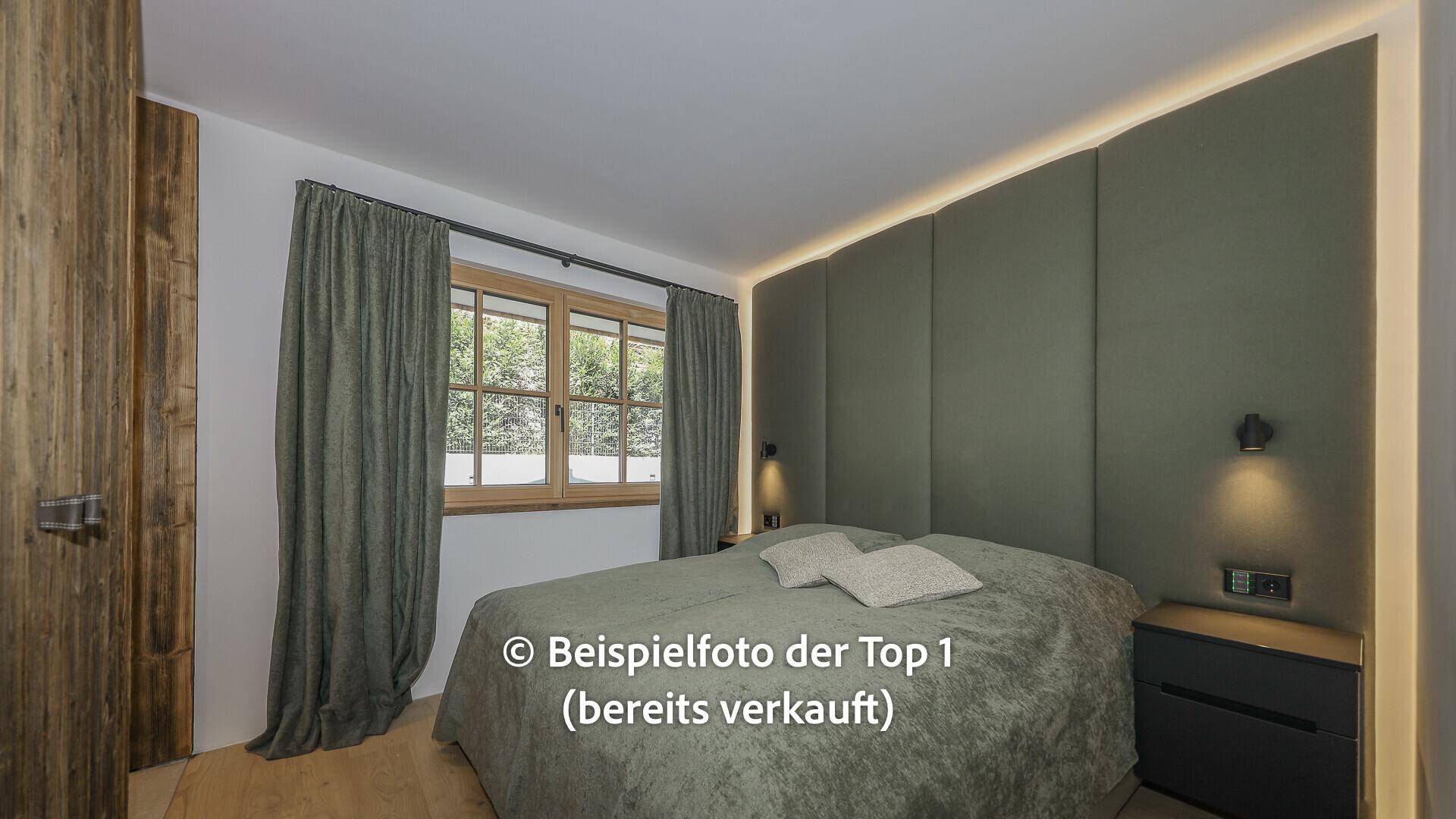 Gemütliches Schlafzimmer mit gepolsterter Wand, Holzboden und Blick ins Grüne.
