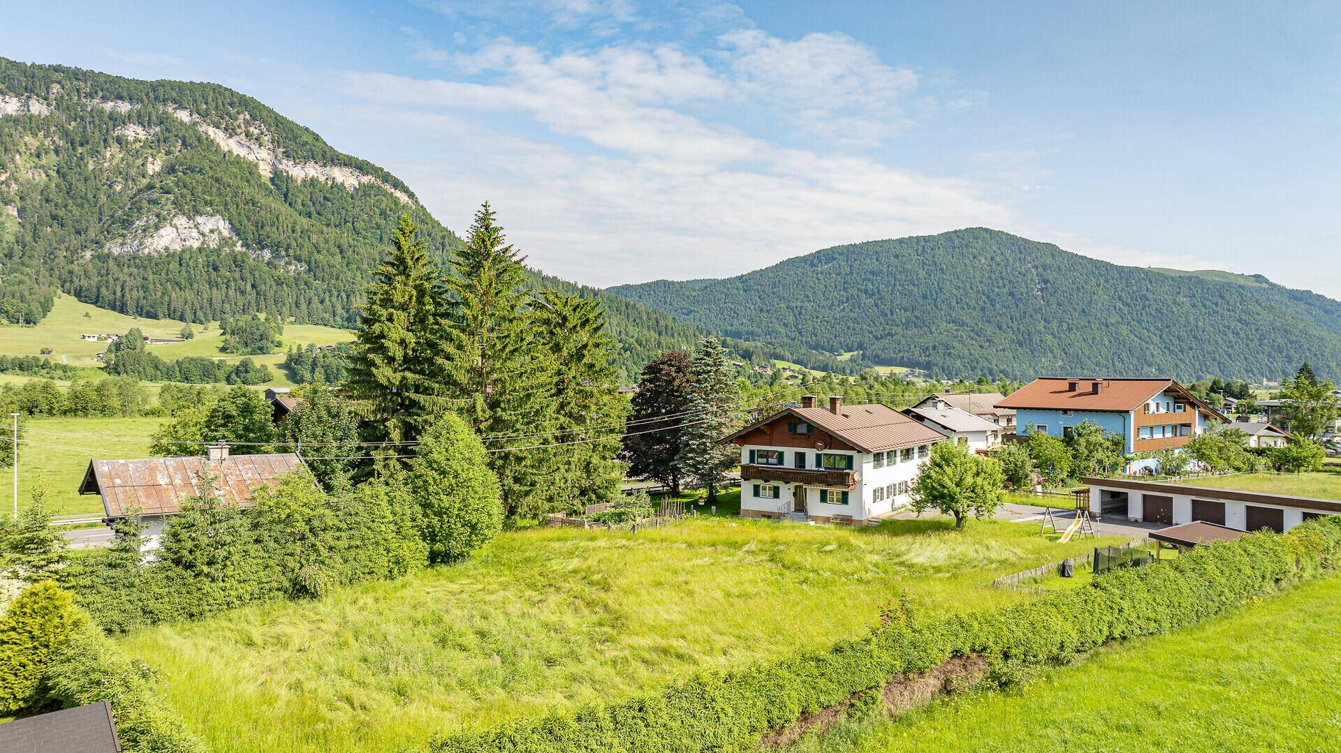 Weitläufige Landschaft mit traditionellen Häusern, grünen Feldern und bewaldeten Bergen.