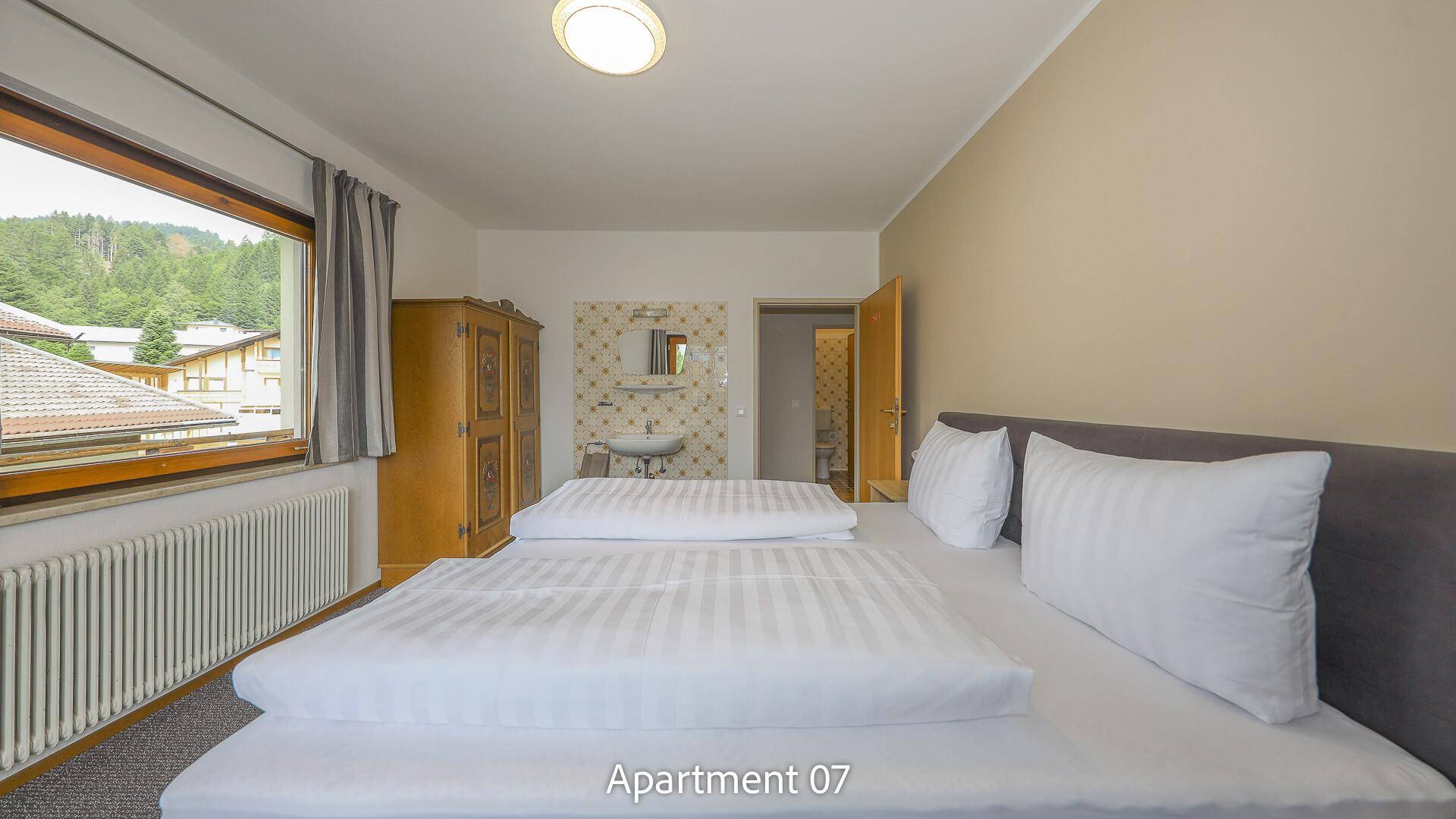 Schlafzimmer von Apartment 07 mit Doppelbett, traditionellem Holzschrank und einem kleinen Waschbecken.
