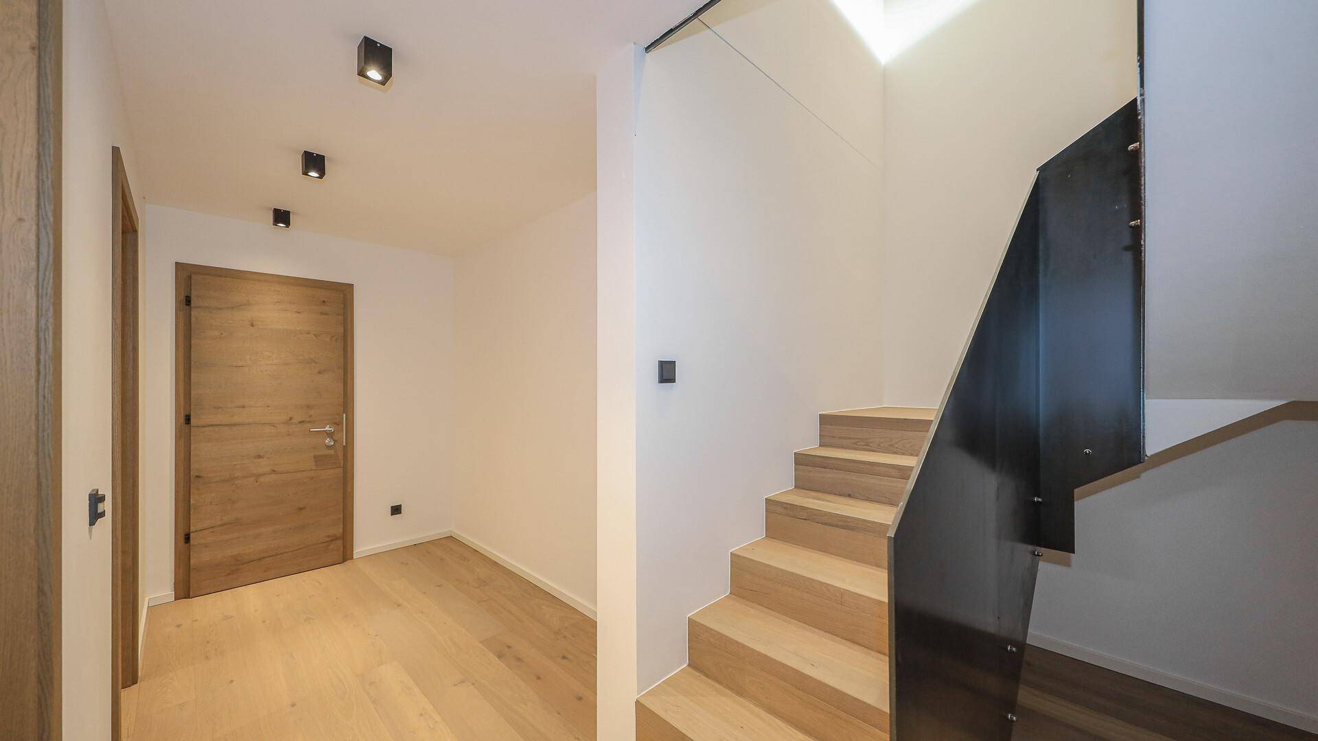 Heller Flur mit Holzboden und moderner Treppe, die in die oberen Etagen führt.