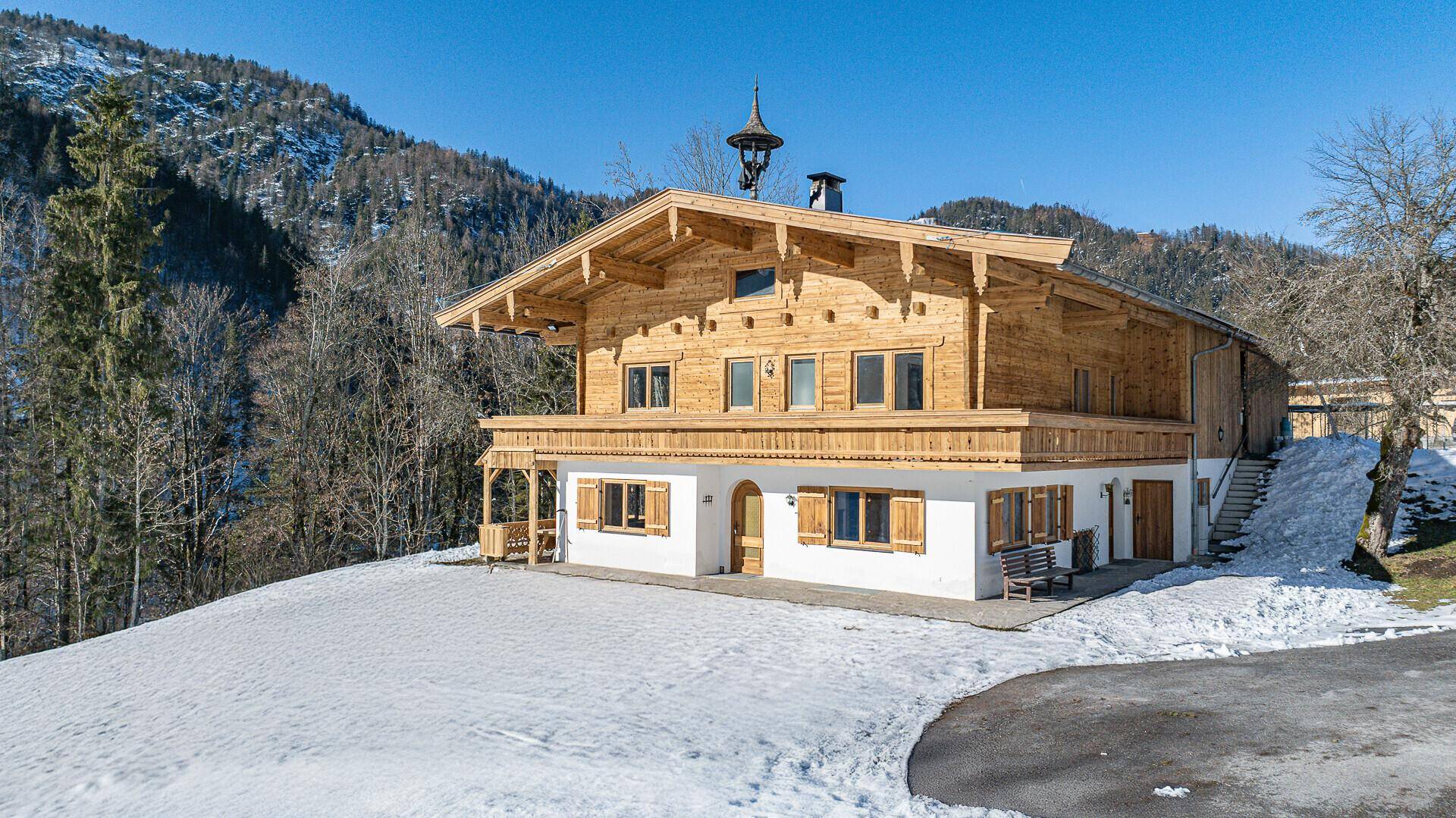 Charmantes Chalet mit Holzfassade und weißen Wänden, umgeben von Schnee und Bergen.