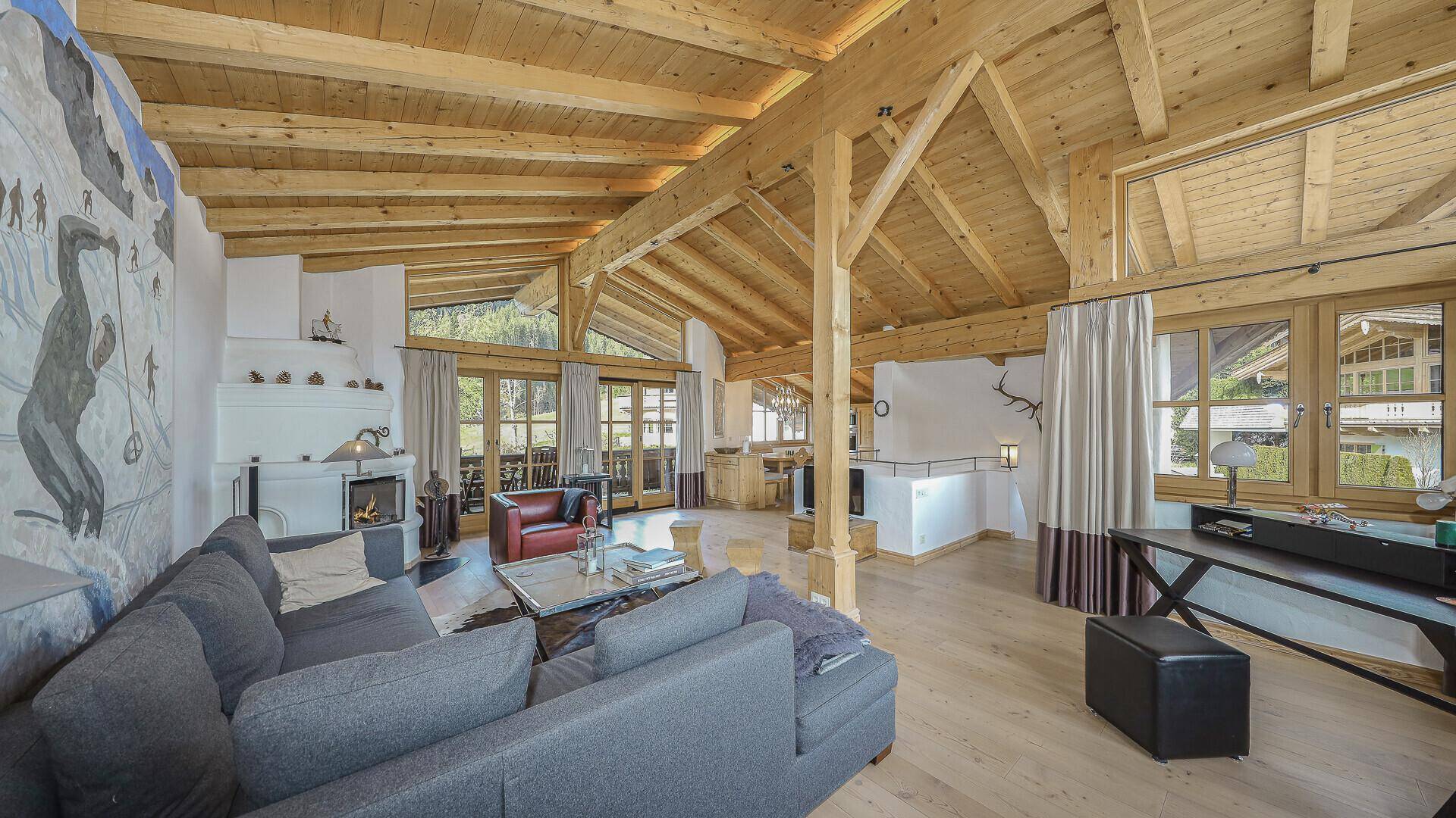 Gemütlicher Wohnbereich mit großem Sofa, Kamin und Holzbalkendecke, offen zur Küche.