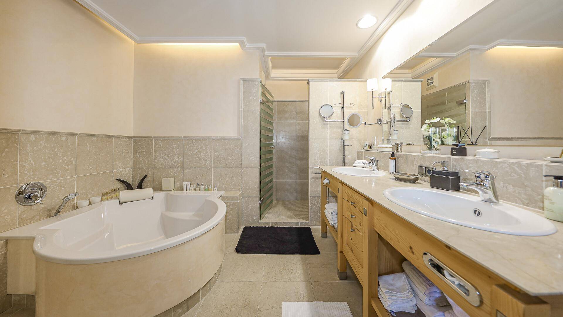 Elegantes Badezimmer mit Doppelwaschbecken, Badewanne und separater Dusche in hellen Fliesen.