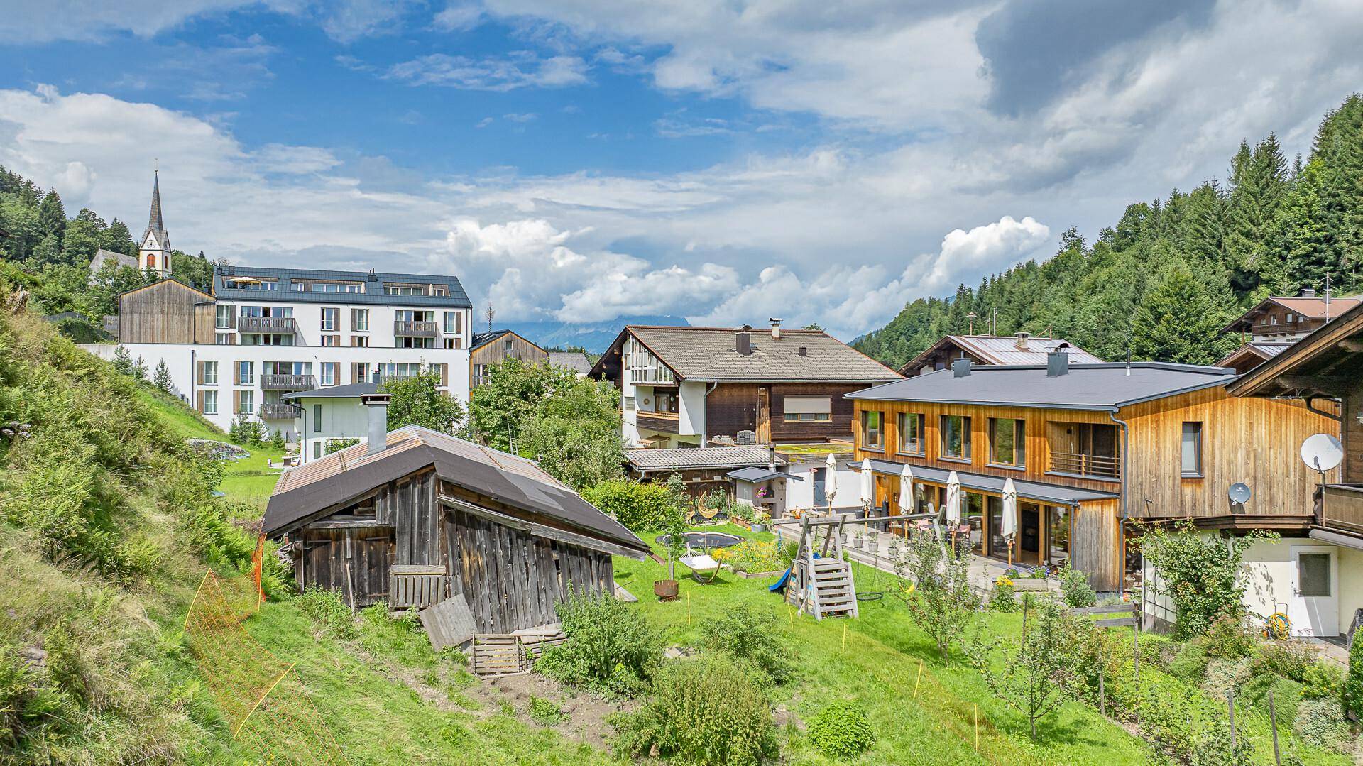 Panoramablick auf die ländliche Umgebung mit mehreren Häusern und einer Kirche im Hintergrund.