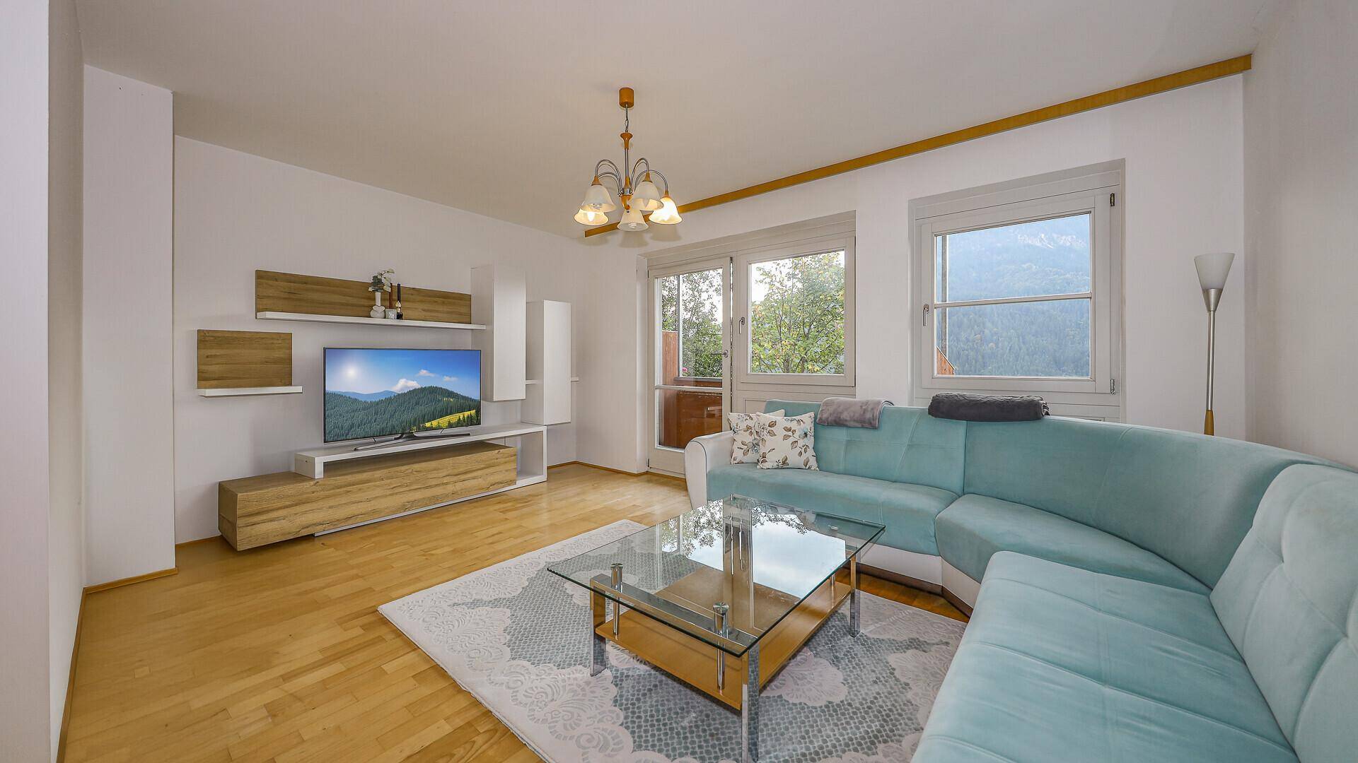 Helles Wohnzimmer mit modernem Sofa, Holzboden und Blick auf die Berge durch große Fenster.