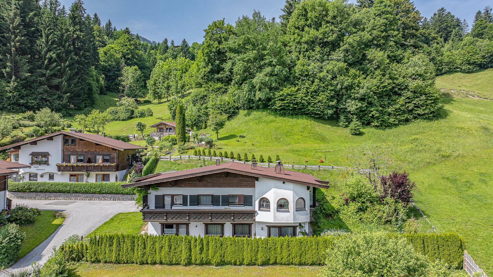 Traditionelles Wohnhaus mit grüner Hecke und Balkon in einer sonnigen Hanglage.