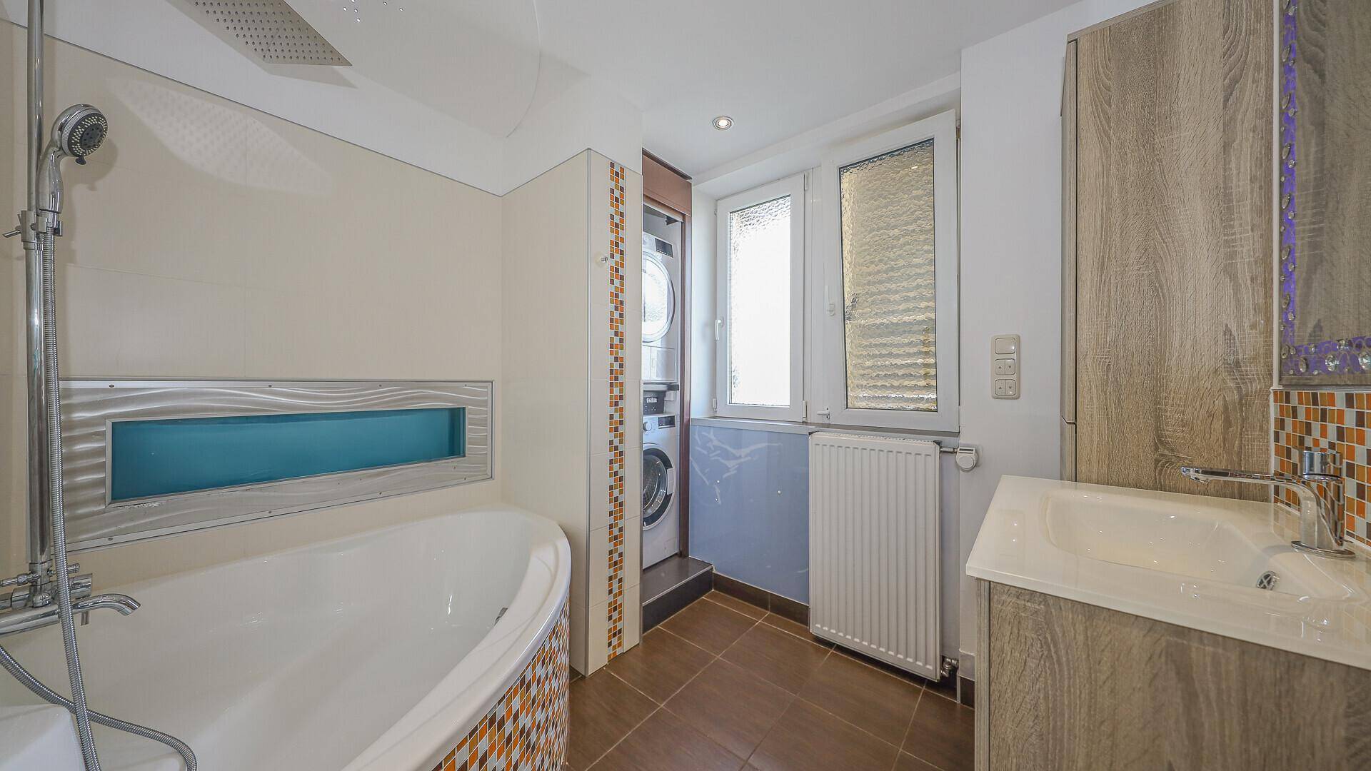 Badezimmer mit Badewanne, Dusche, Waschbecken und Waschmaschine, mit Fenster für Tageslicht.