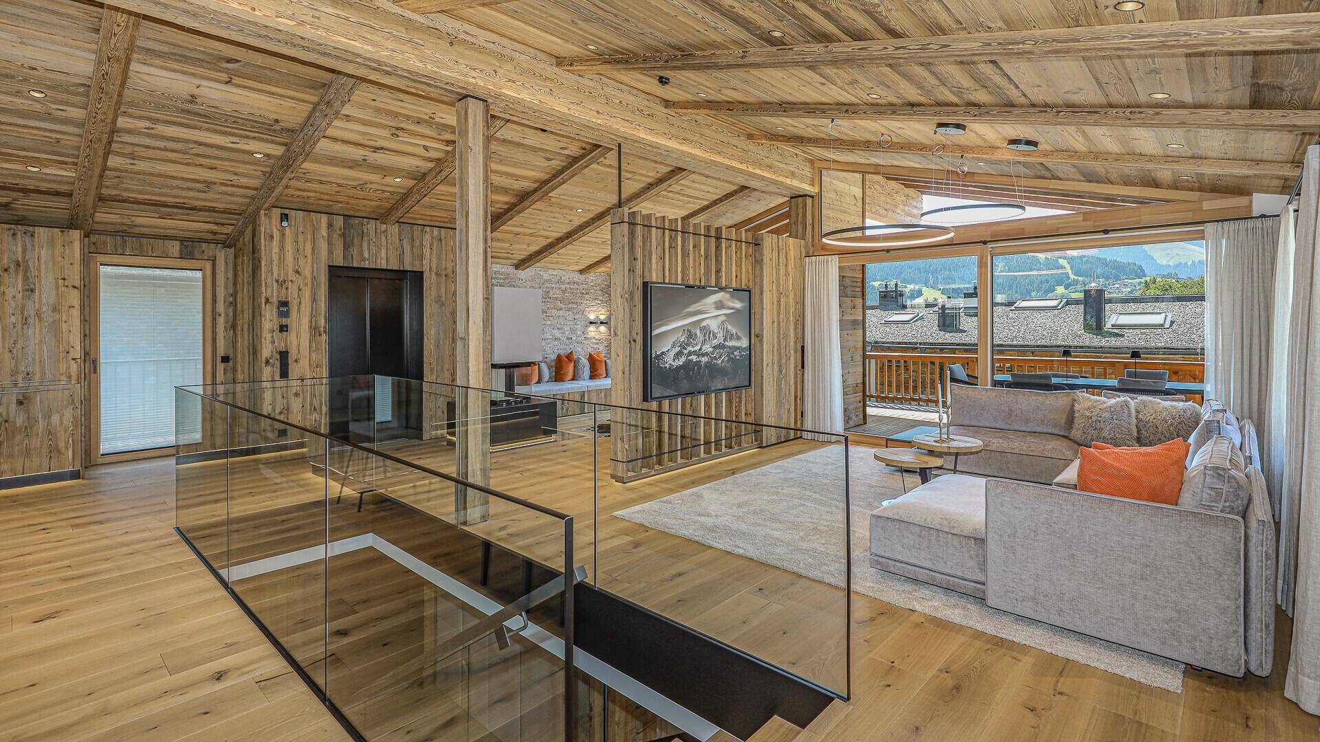 Heller Wohnbereich mit Holzelementen, Glasgeländer und Zugang zum Balkon mit Bergblick.