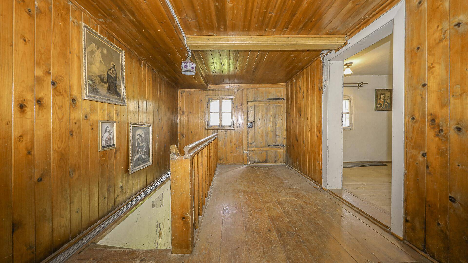 Rustikaler Flur im Obergeschoss mit Holzverkleidung, Holzdielenboden und traditionellen Bildern.