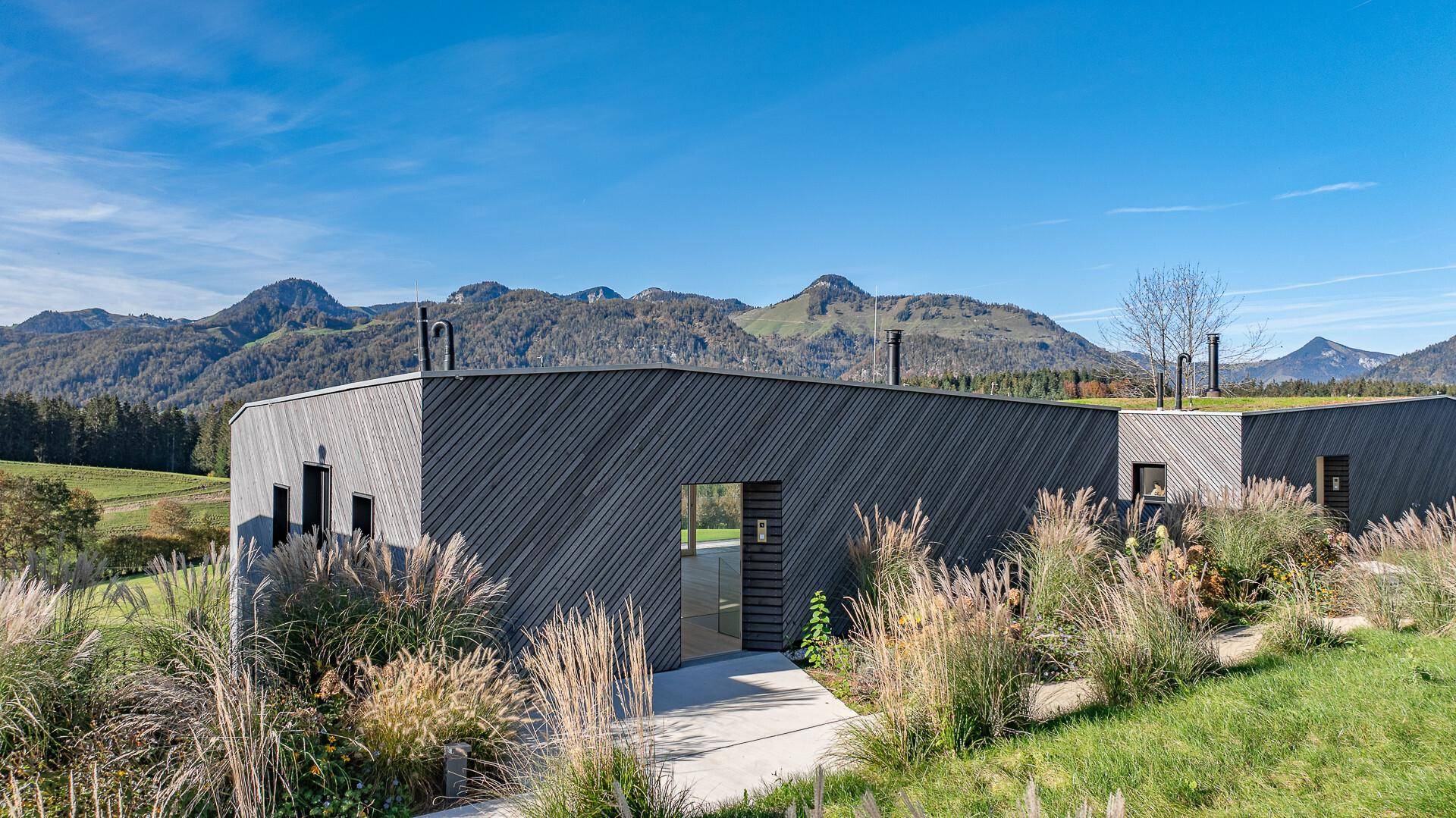 Moderne Architektur mit Holzfassade, umgeben von üppiger Vegetation und Bergblick.