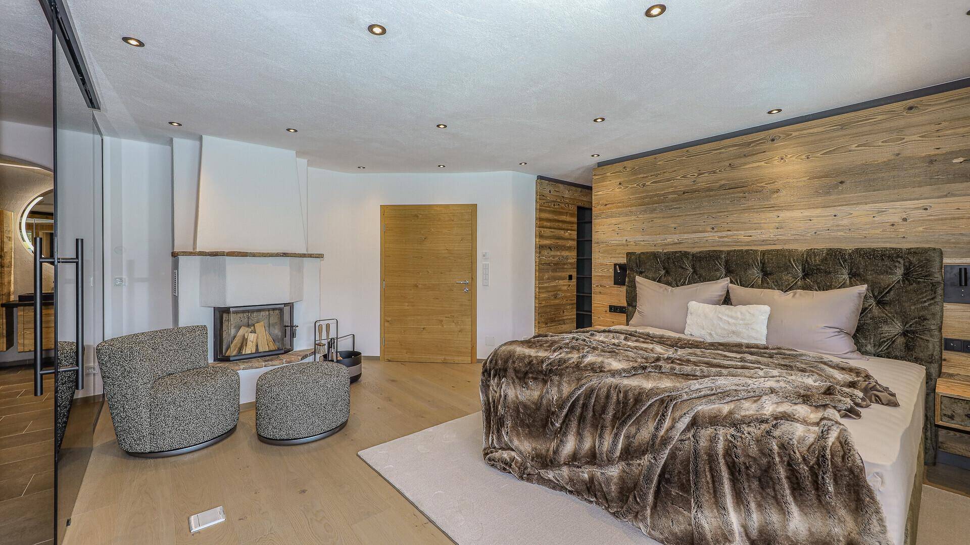 Elegantes Schlafzimmer mit Kamin, Holzwand und großem Doppelbett für höchsten Komfort.