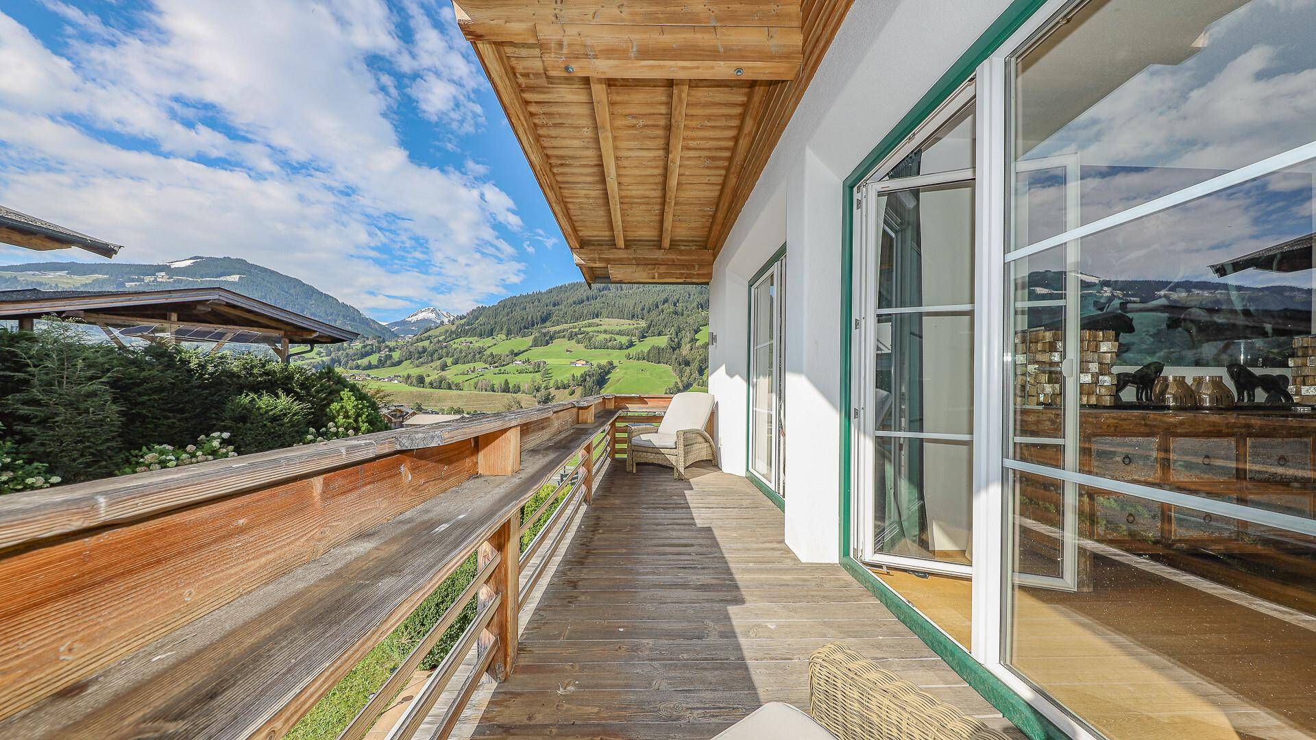 Langer Holzbalkon mit Bergblick und Sitzgelegenheiten, ideal zum Entspannen in der Natur.