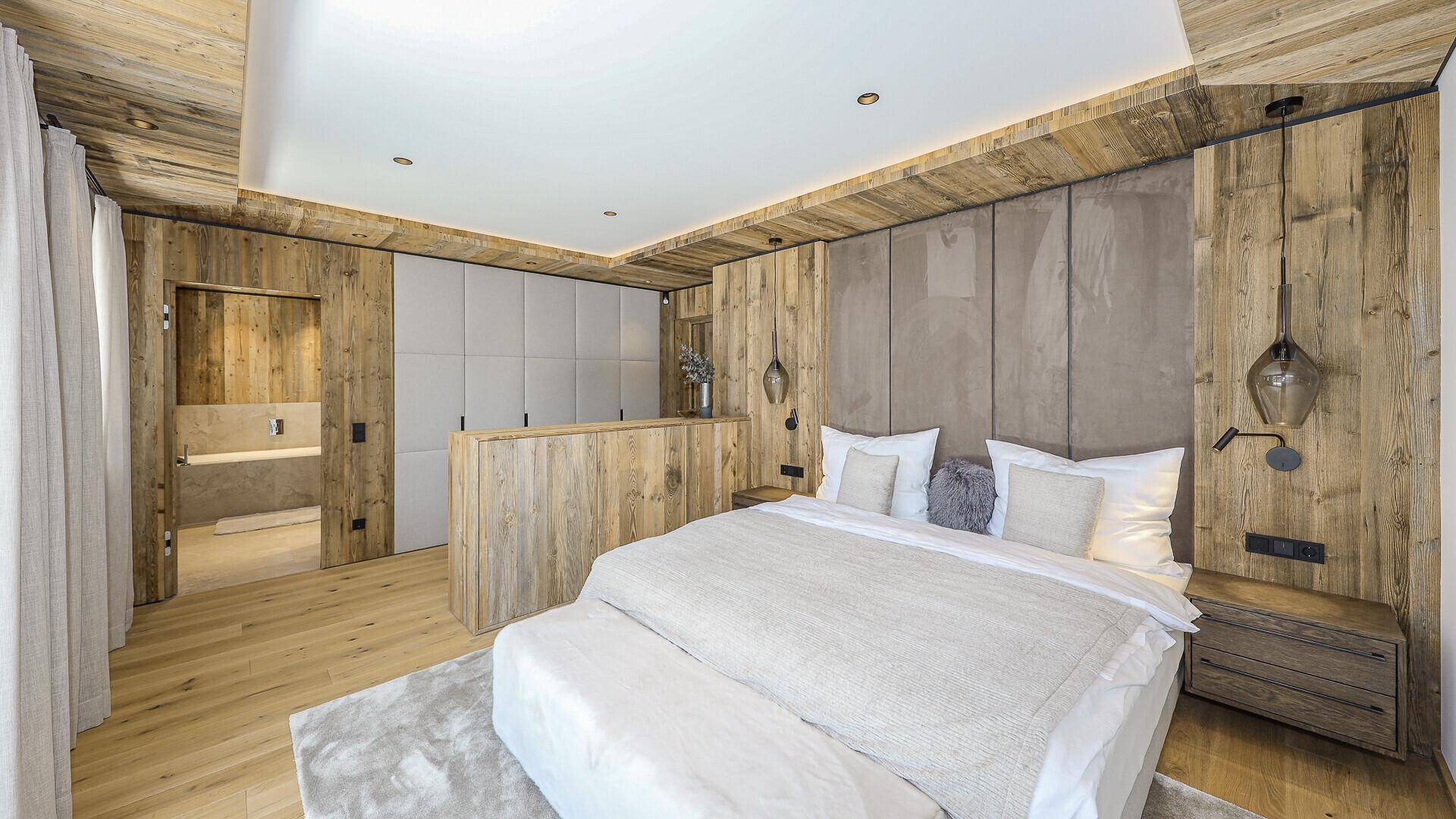 Elegantes Schlafzimmer im alpinen Stil mit Holzwänden, Doppelbett und Zugang zum Bad.