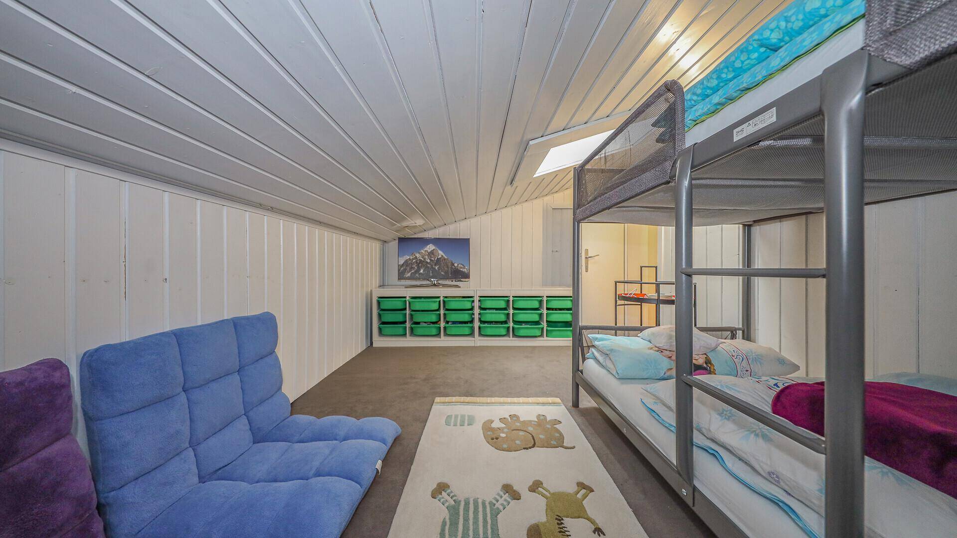 Kinderzimmer im Dachgeschoss mit Etagenbetten, blauem Sofa und schräger Holzdecke.