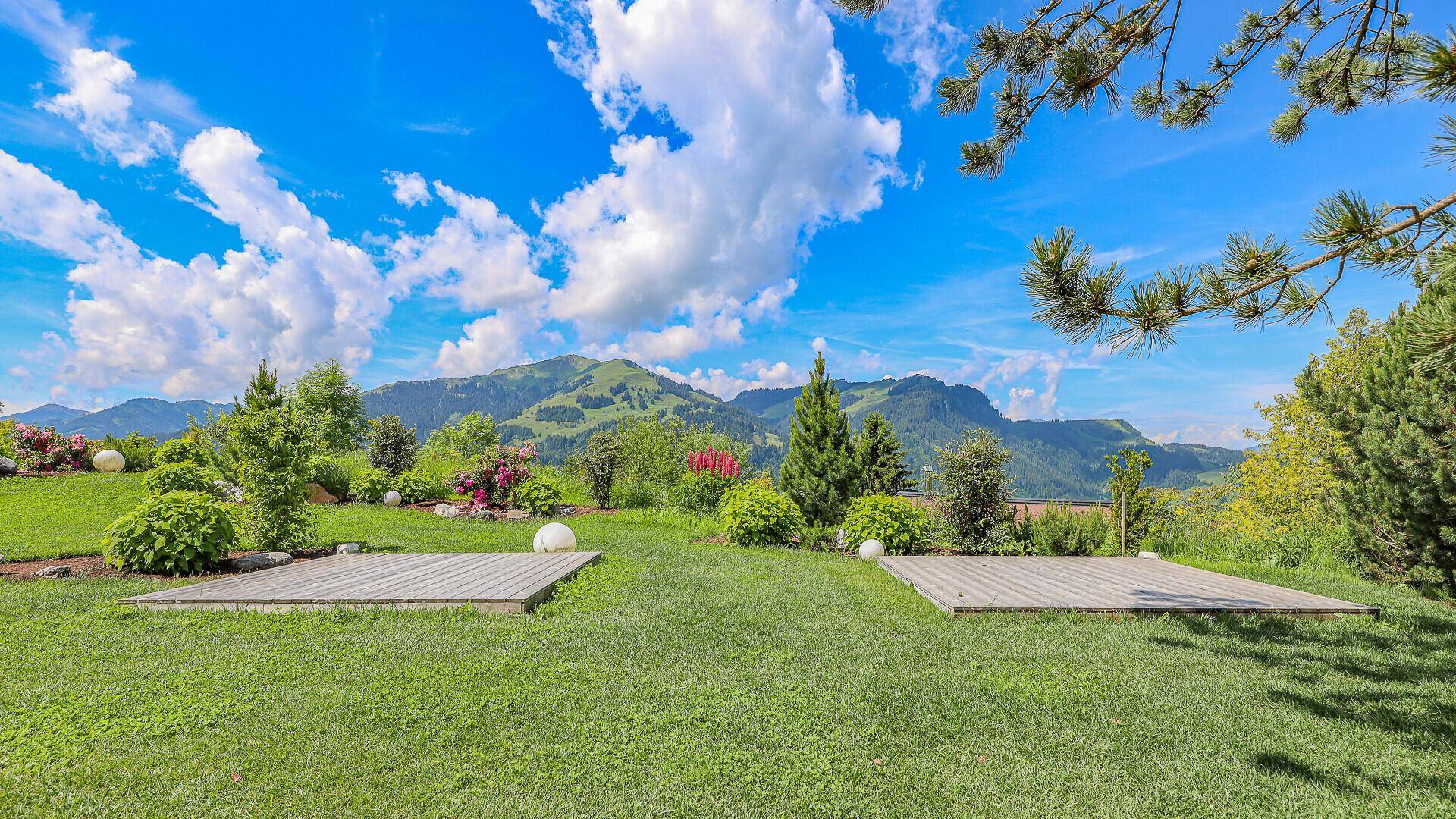 Gepflegter Garten mit Rasenflächen, Holzdecks und Panoramablick auf die Berge.